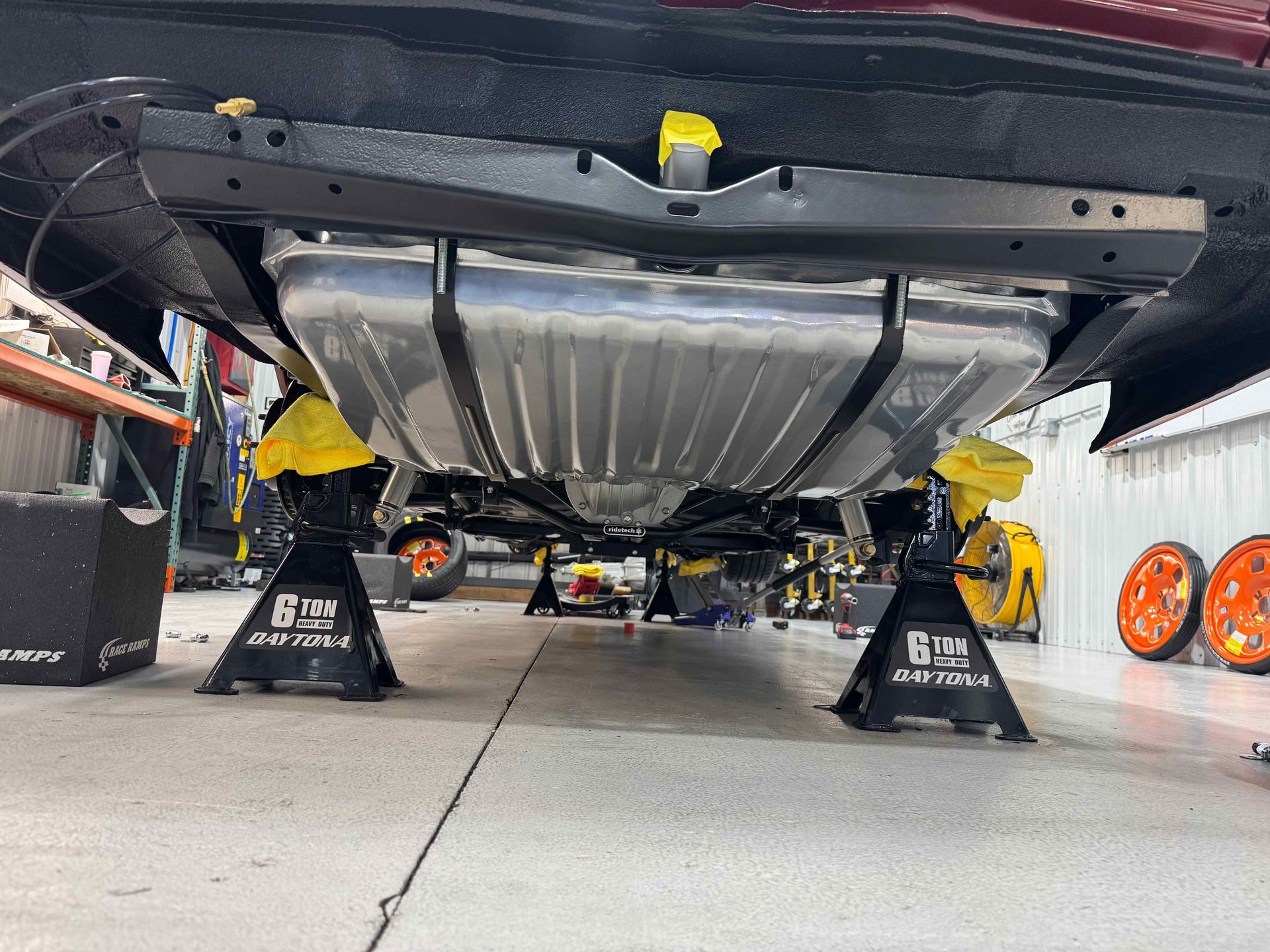 Undercarriage of a car lifted on jack stands in a garage with yellow wheel chocks visible.