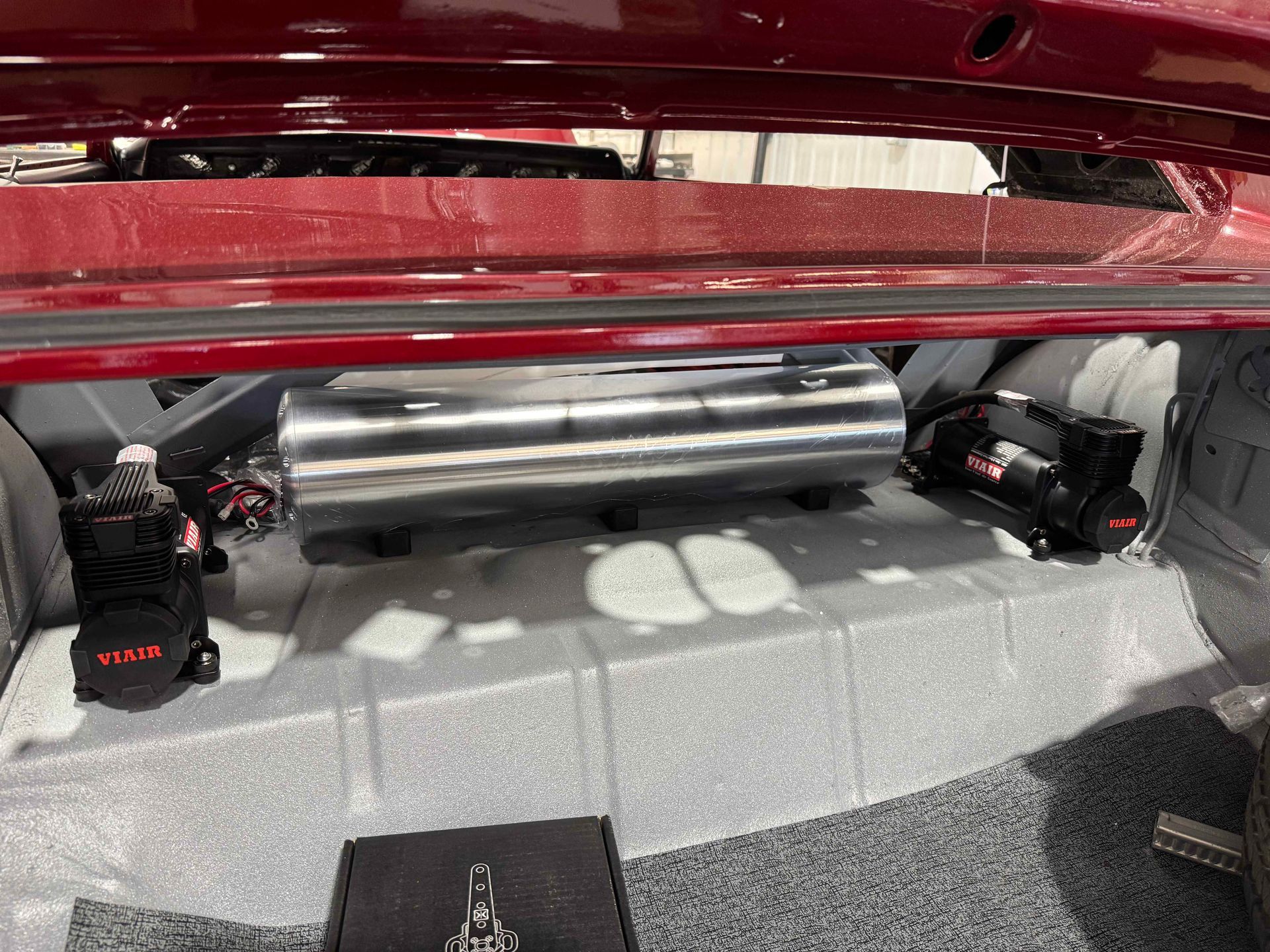 Car trunk with a chrome subwoofer box and two black KICKER speakers on a gray carpeted floor