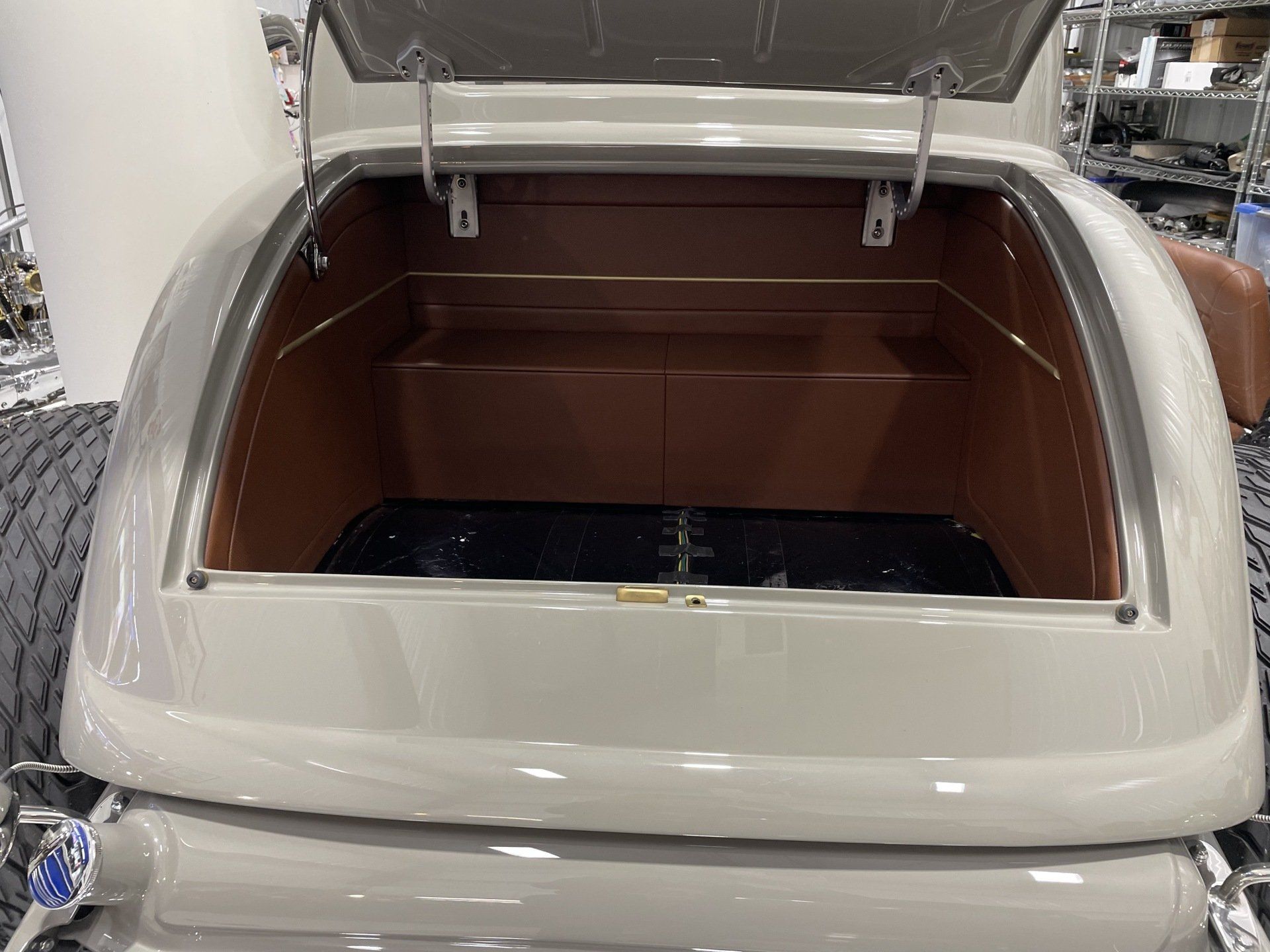 Open vintage car trunk with beige exterior and brown interior, viewed from the rear