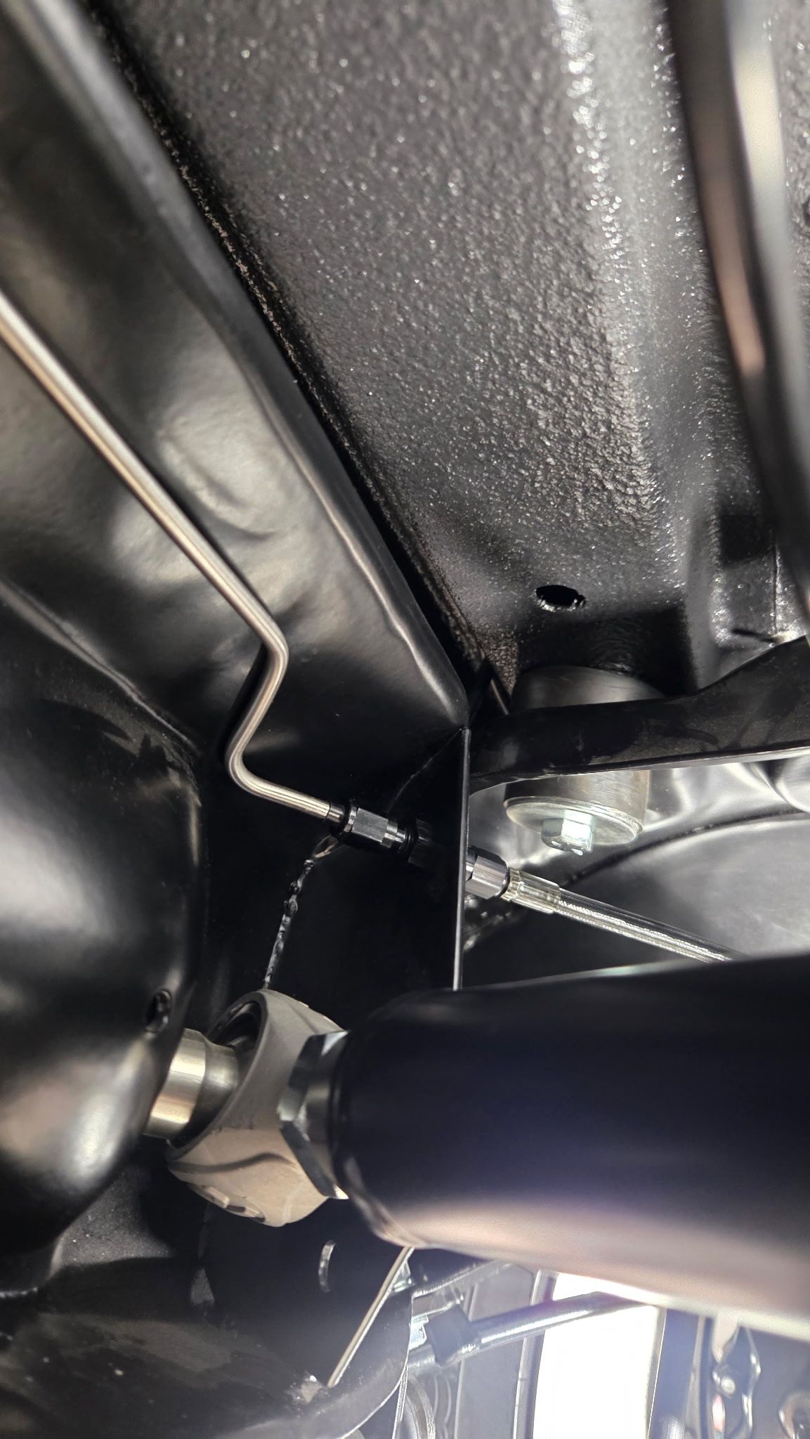 Close-up of black vehicle undercarriage with metal frame, bolts, and a pipe or suspension component