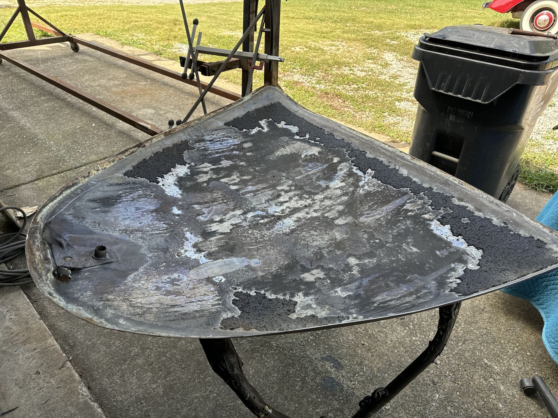 Black metal table with peeling paint on a patio beside a trash bin and grassy yard