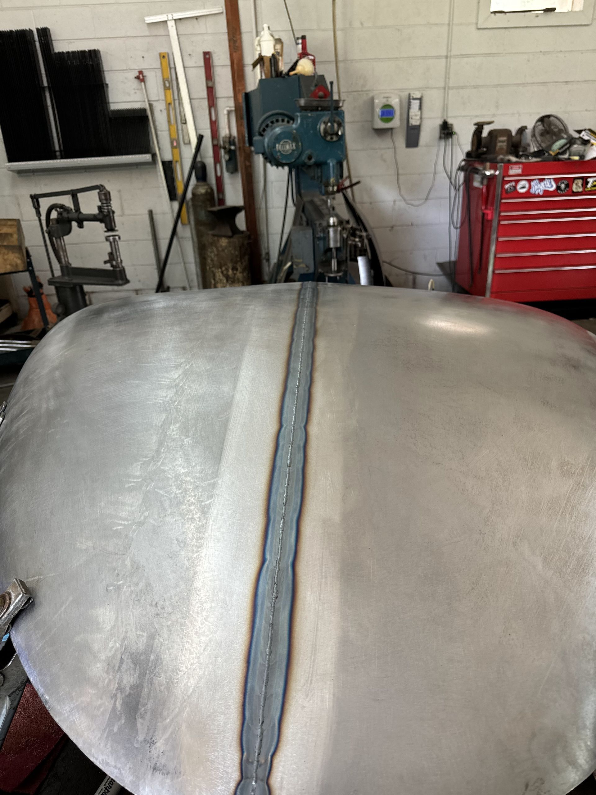 Large metal hood or tank in a workshop, with tools and machinery in the background.