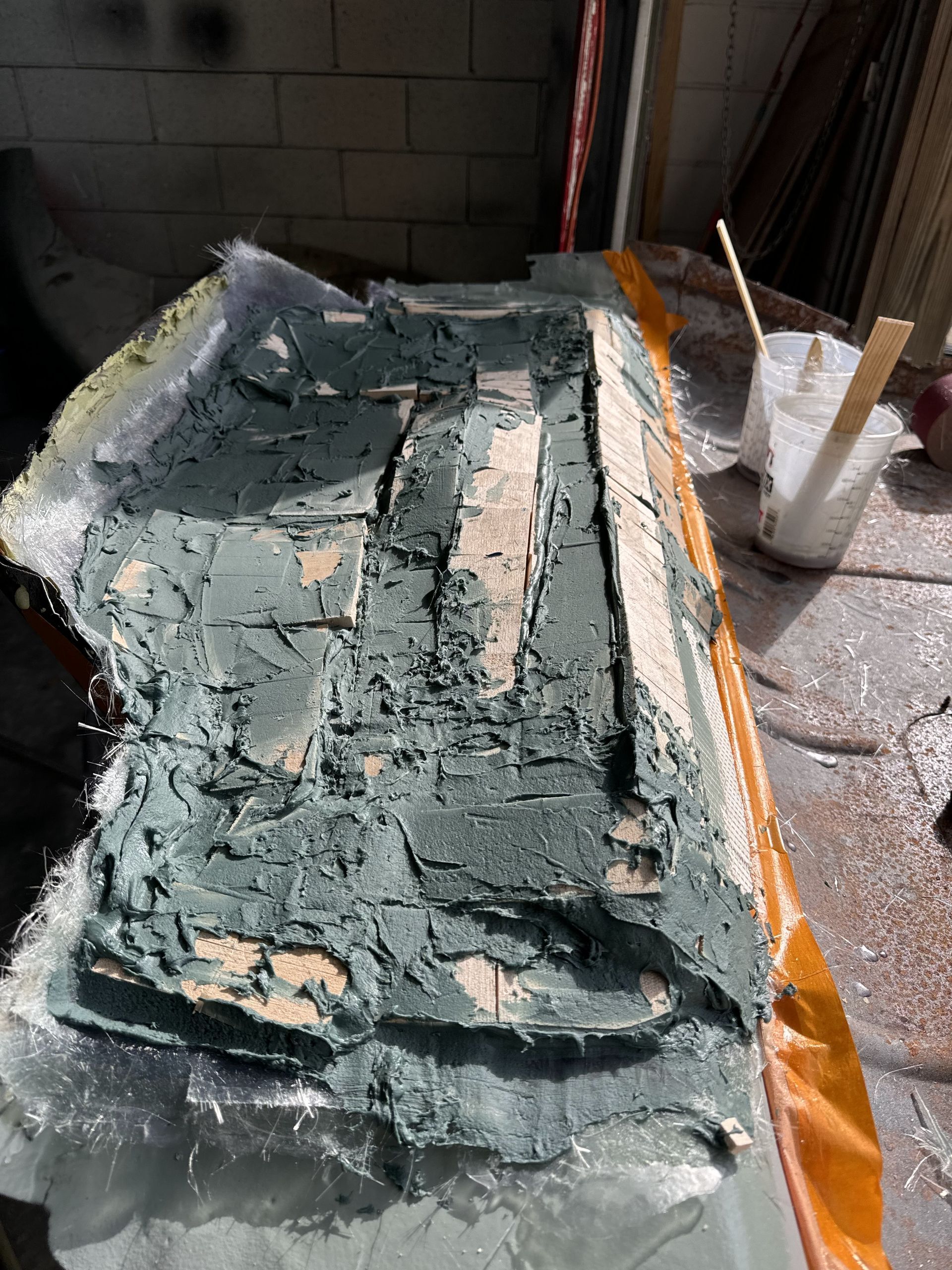 Damaged green-painted surface with peeling layers, surrounded by debris and orange tape in a workshop area