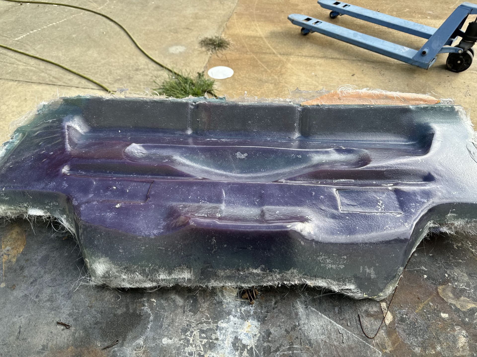Purple plastic sled or tub lying on concrete outdoors near a cart.