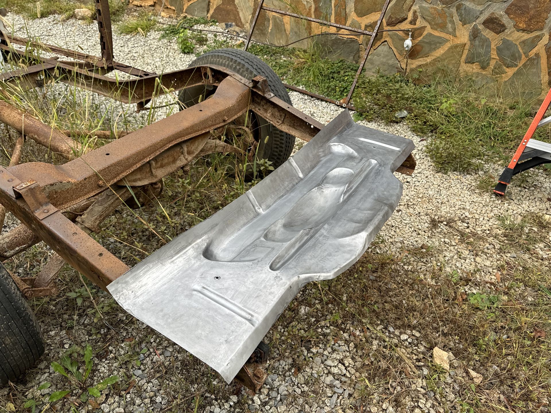 Crushed silver car body panel on a rusty frame in a gravel yard