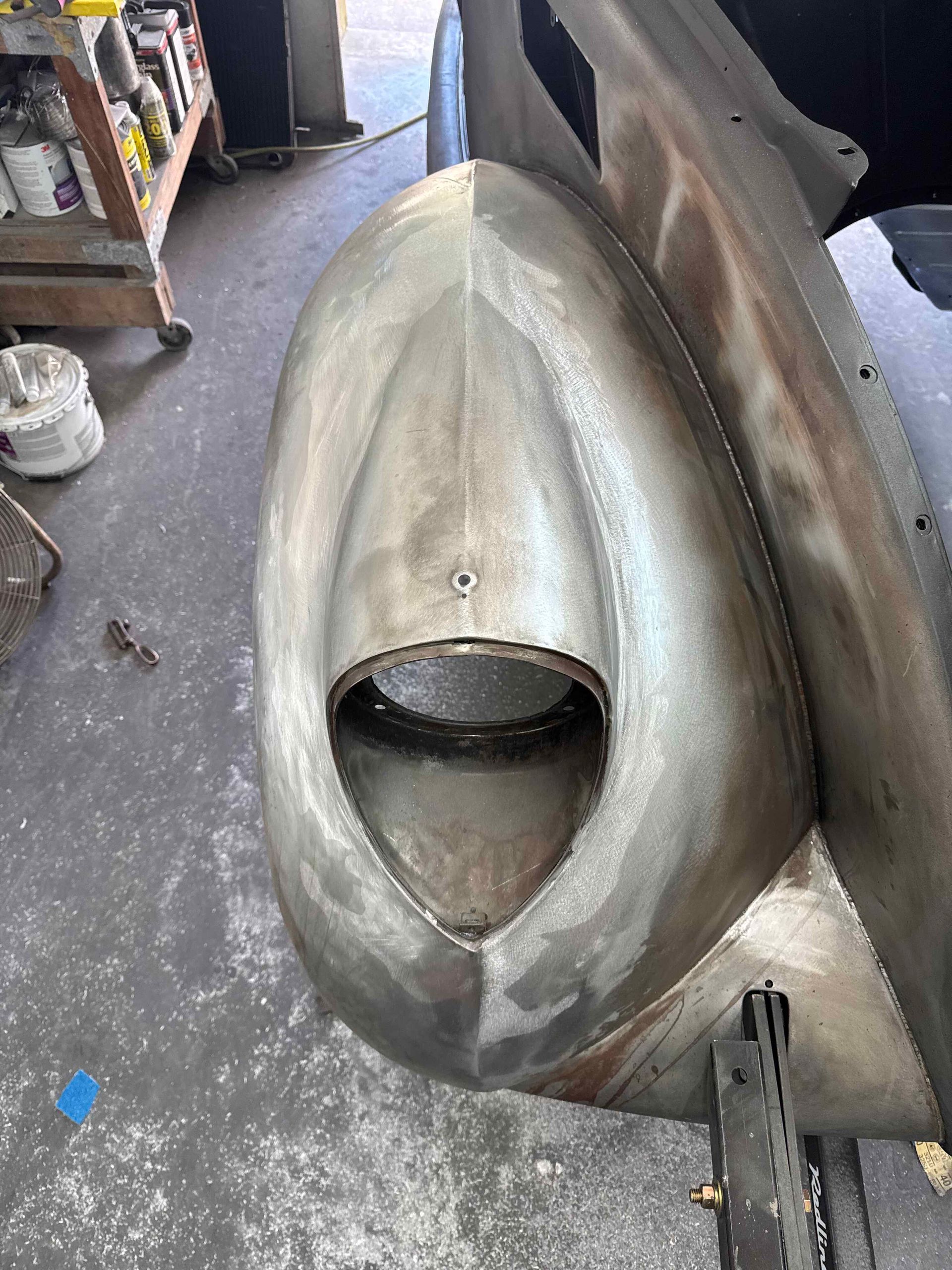 Large oval metal object with a central opening, shown in a workshop on a concrete floor.