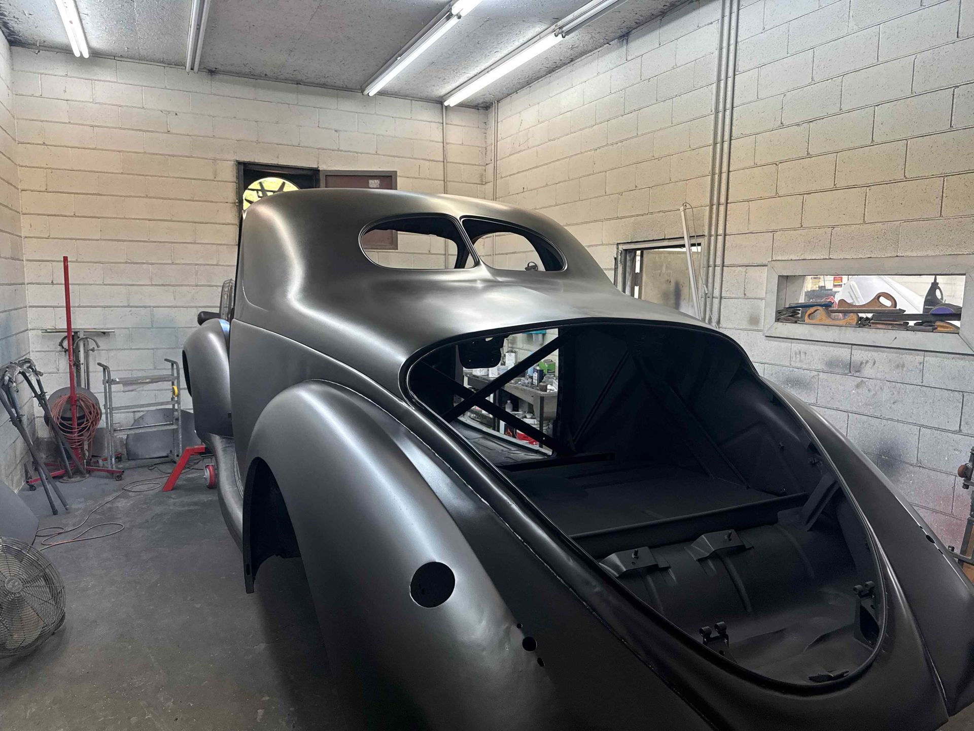 Classic car body in a workshop, partially restored and painted metallic gray, with rear hatch open.