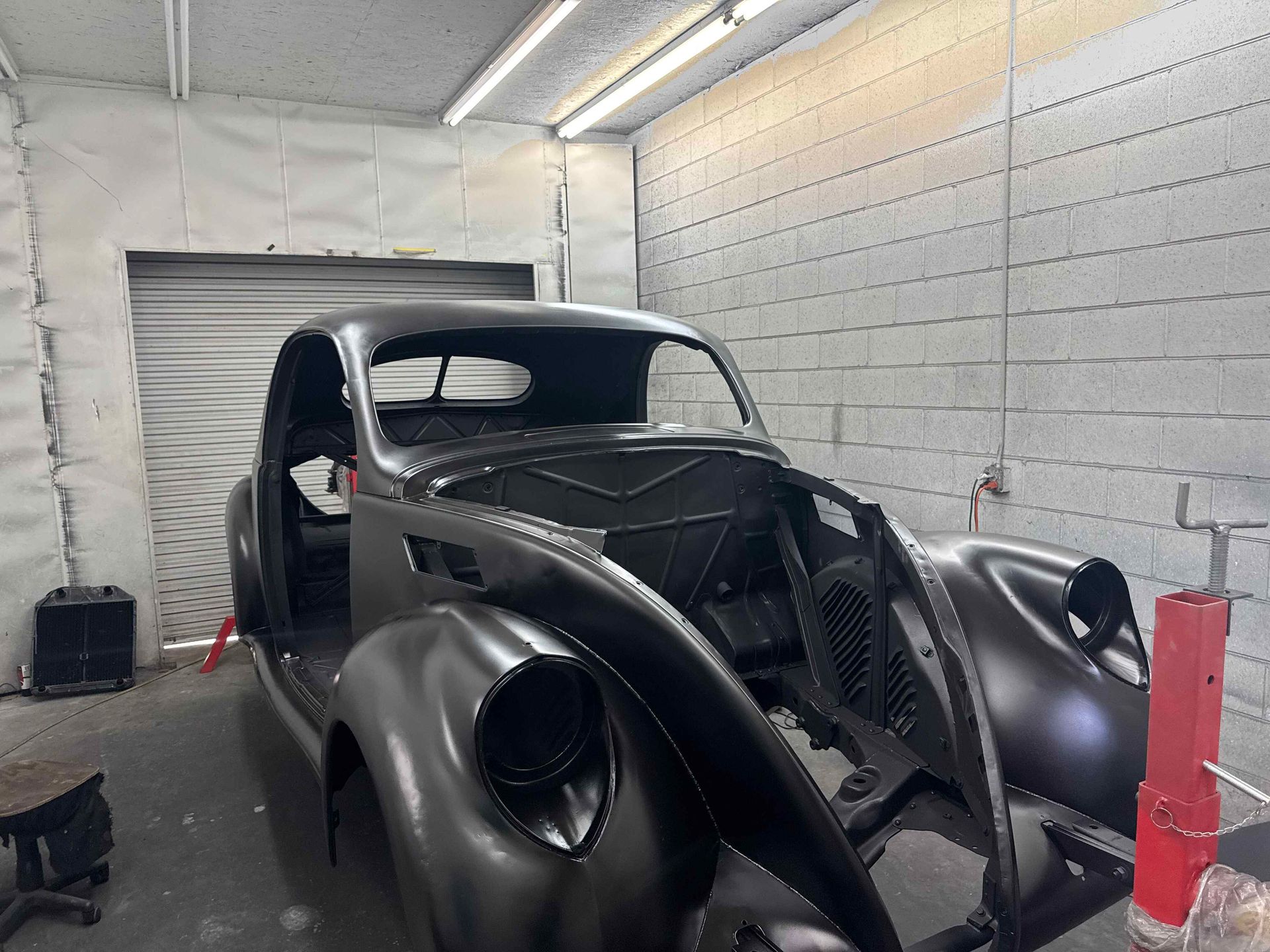Black classic car body shell in a white auto shop garage with an unfinished front end.