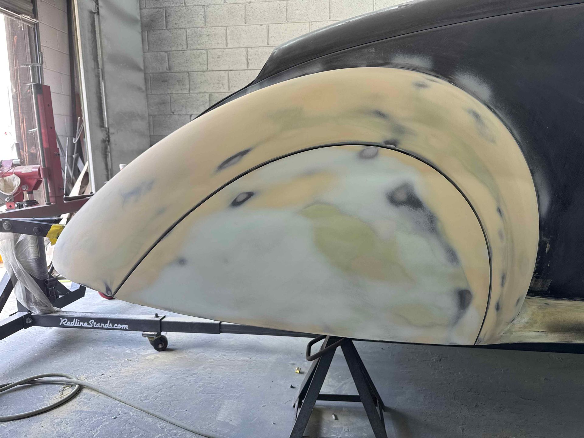 Large cream-colored curved body panel under construction in a workshop, propped on a stand, with sanding marks visible