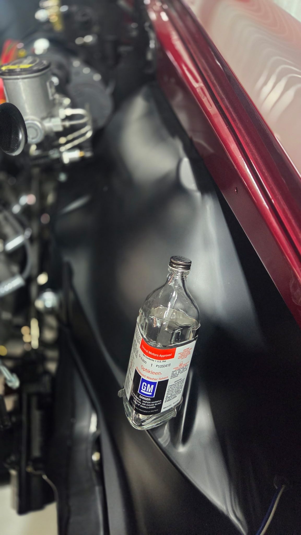Water bottle lying on a dark car floor beside a red-trimmed seat and mechanical parts