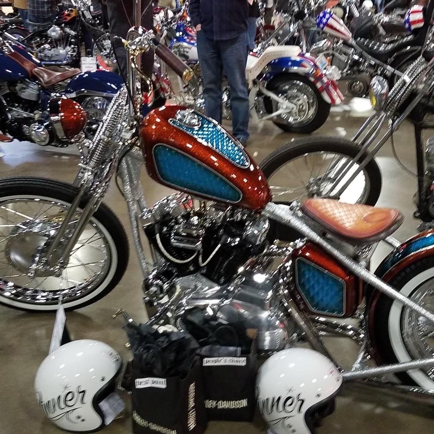 Chrome custom motorcycle with red and blue paint at an indoor bike show, surrounded by other bikes