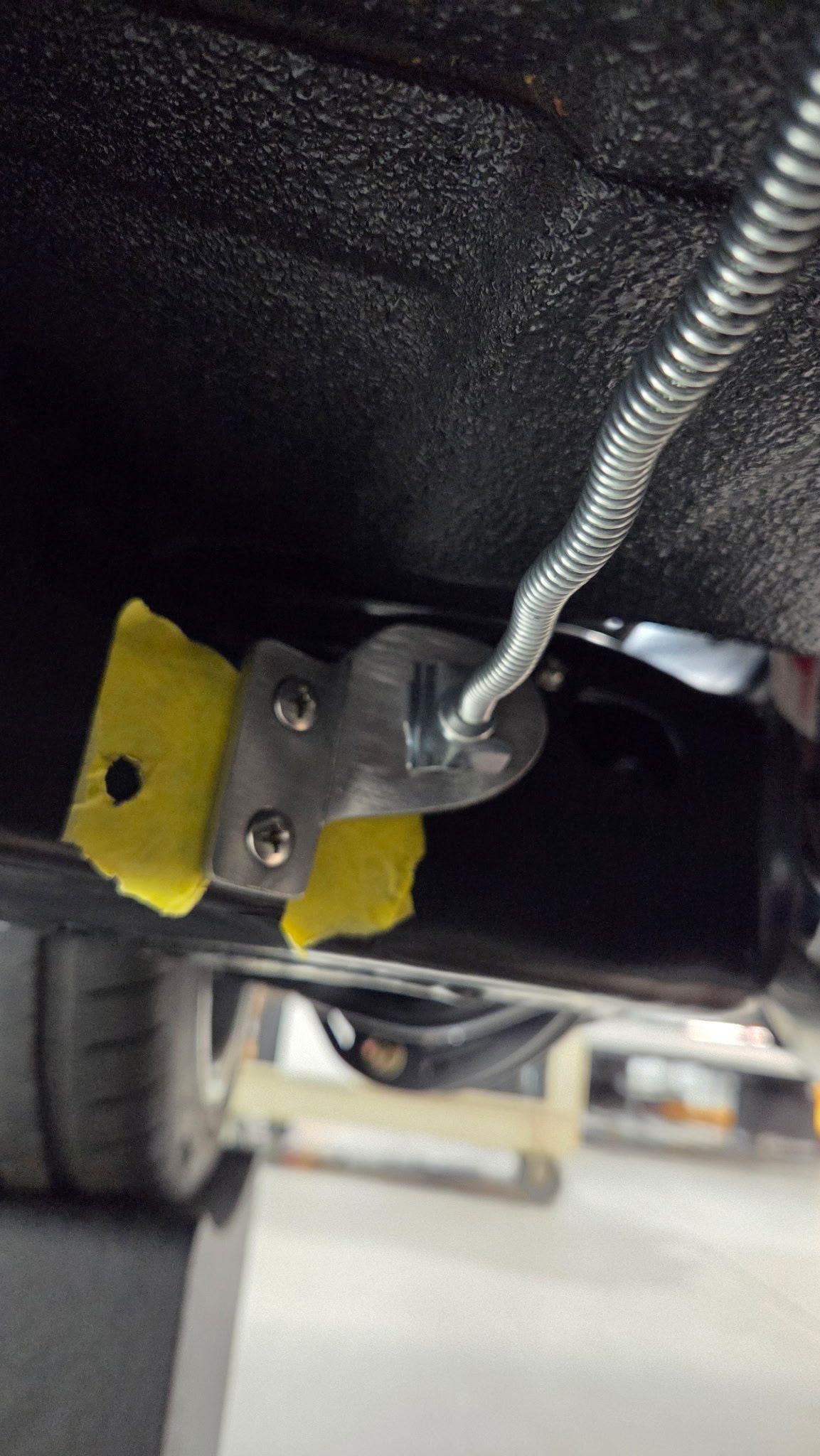Close-up of a yellow electrical connector mounted under a vehicle with a flexible metal conduit attached