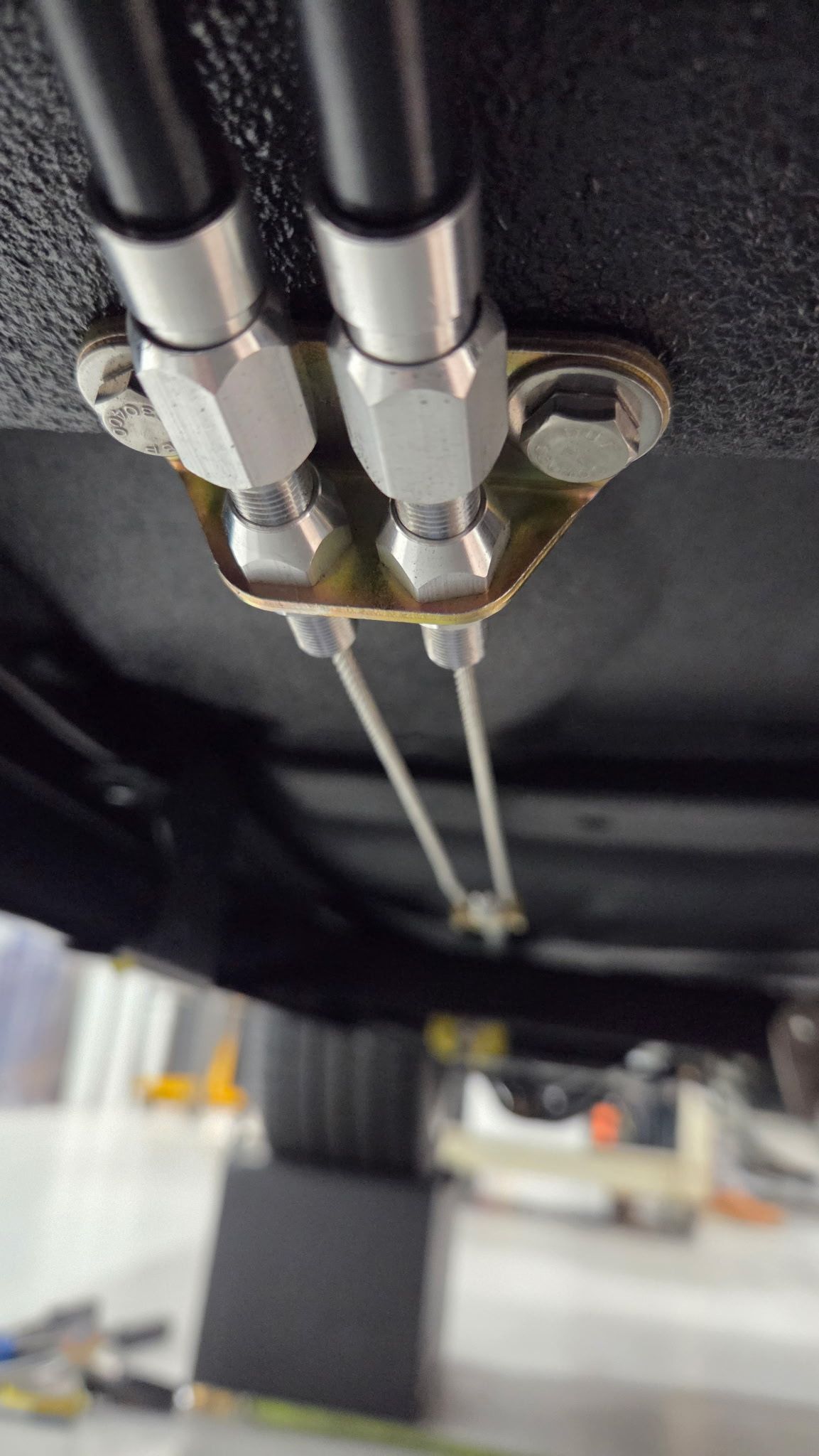 Close-up of two metal hoses and fittings connected to a bracket beneath a vehicle.