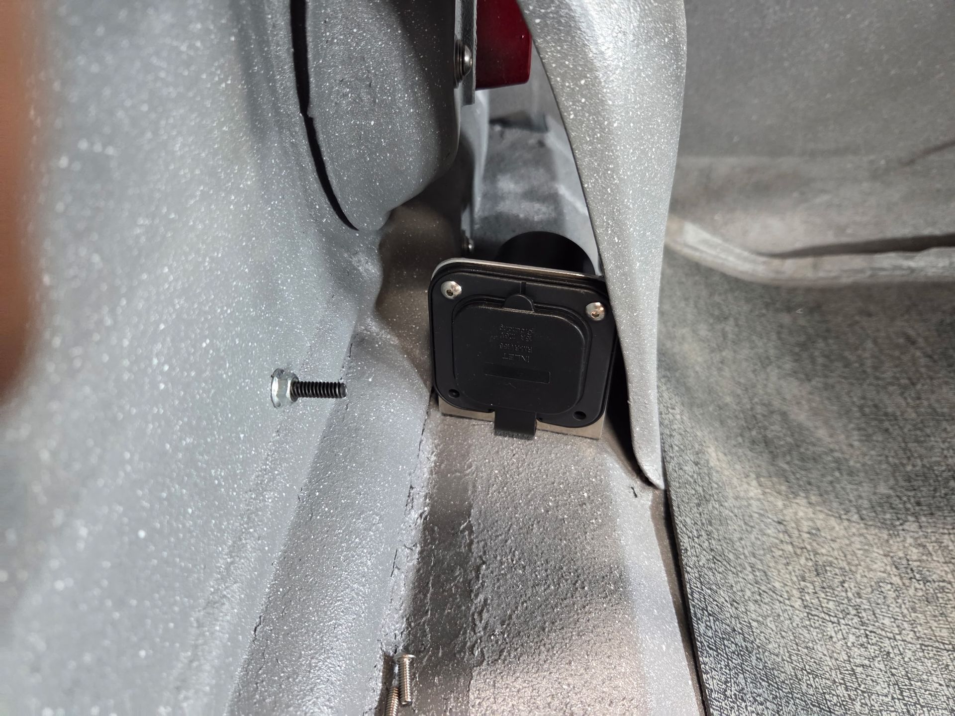 Close-up of a car seat latch mechanism between gray upholstery panels.