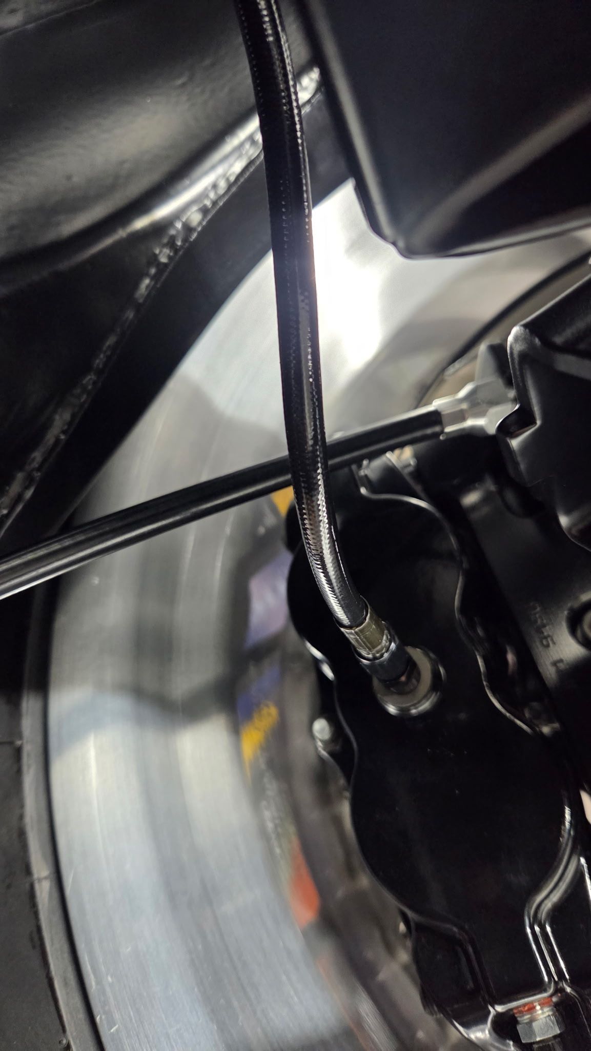 Close-up of a bicycle brake mechanism with a cable and black components near the wheel.