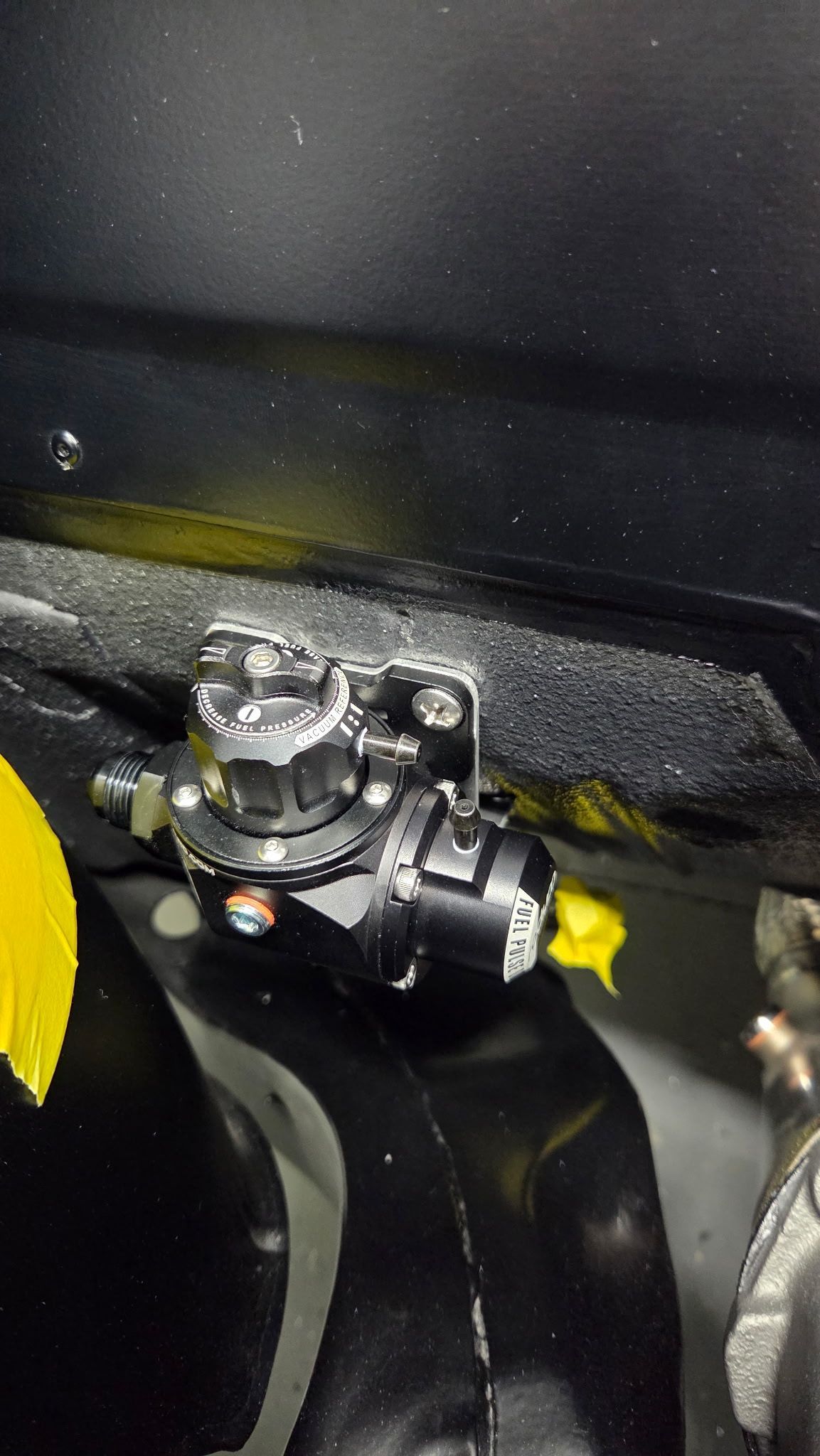 Close-up of a shiny metal latch on a black surface with yellow tape nearby.