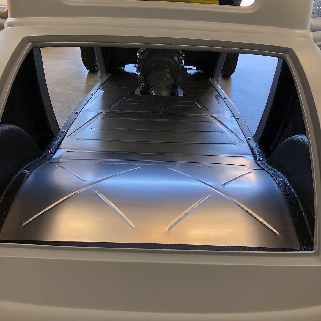 Open vehicle cargo area with a silver folded load floor and rear tires visible in the background