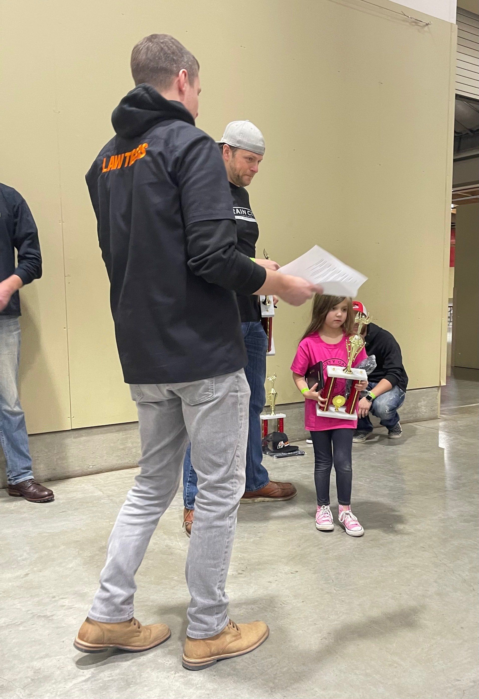 Adult handing papers to child in a hallway, with another adult nearby.