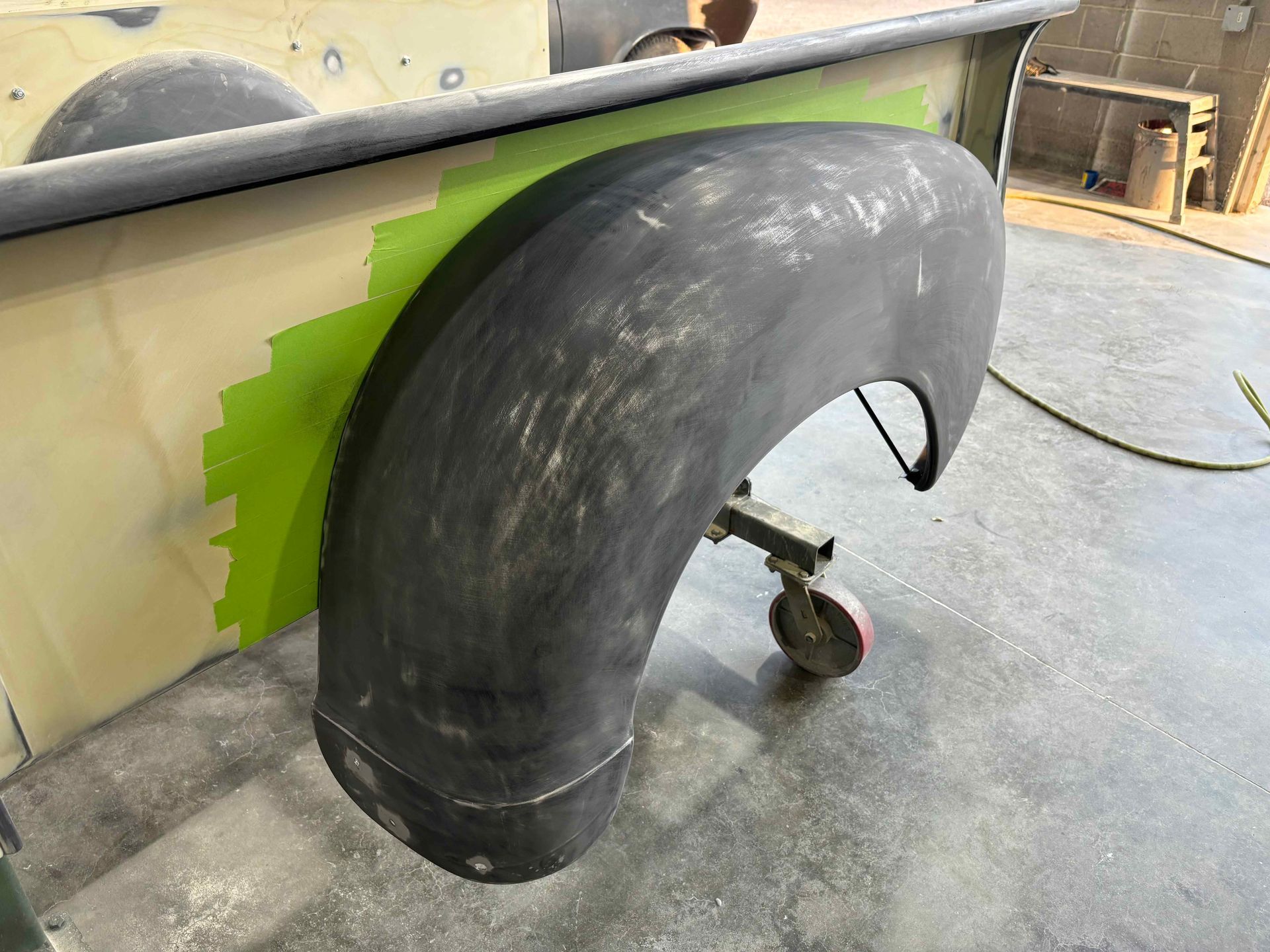 Black curved fender attached to a boat hull in a workshop, with green masking tape visible underneath.