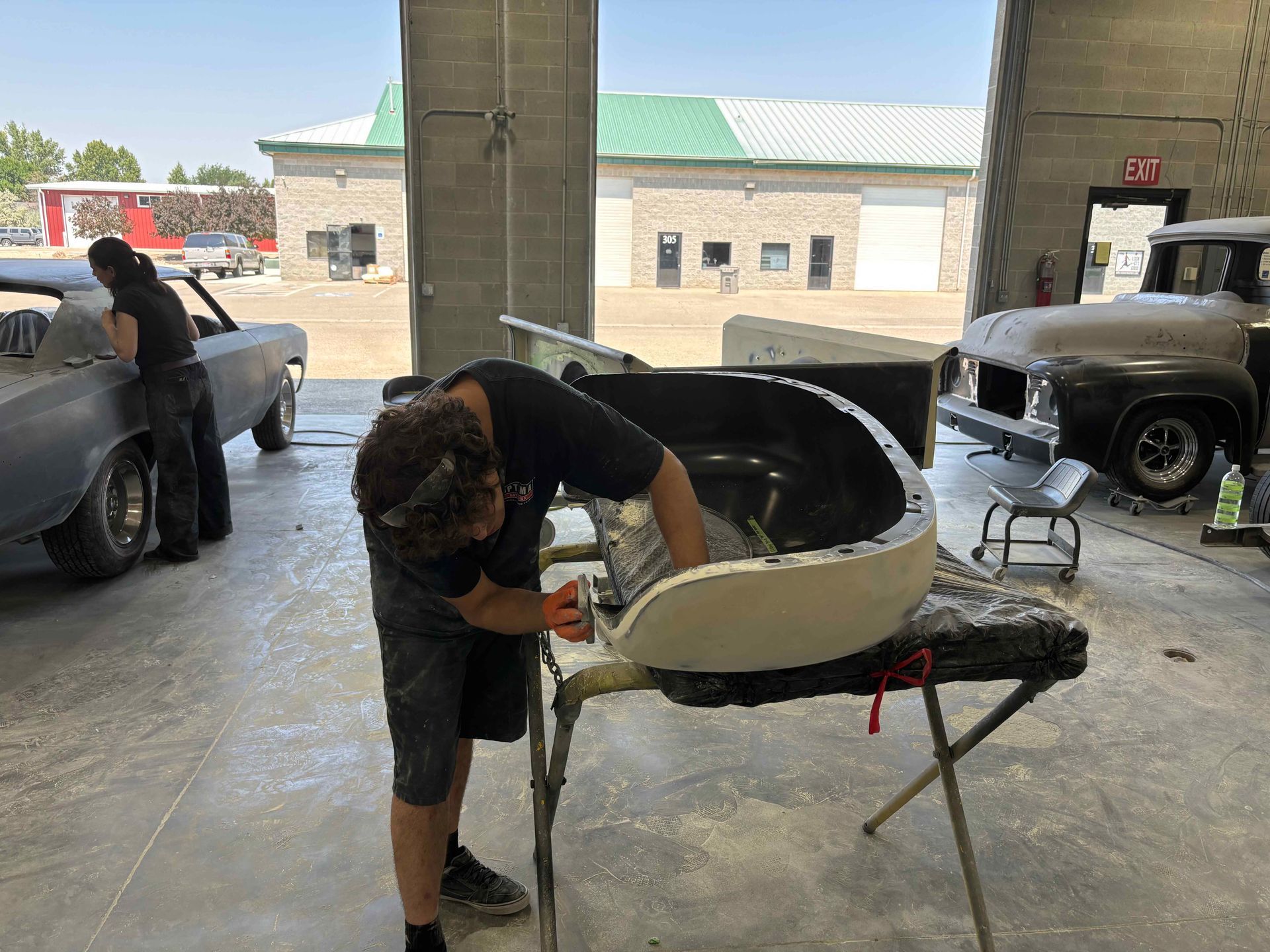 Person sandblasting a cream-colored car body in a workshop garage