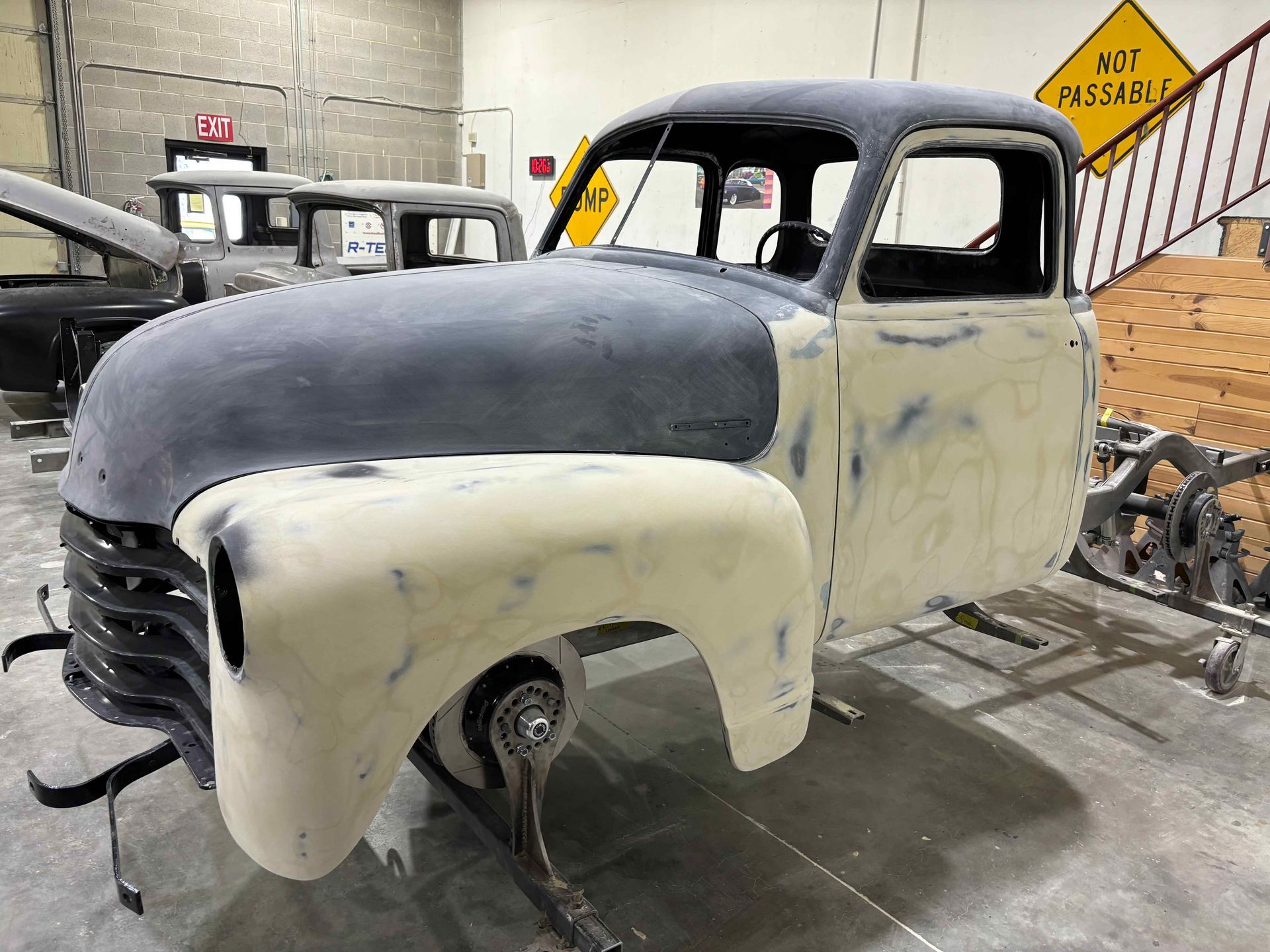 Partially restored vintage truck cab with cream fenders and black hood in a workshop.