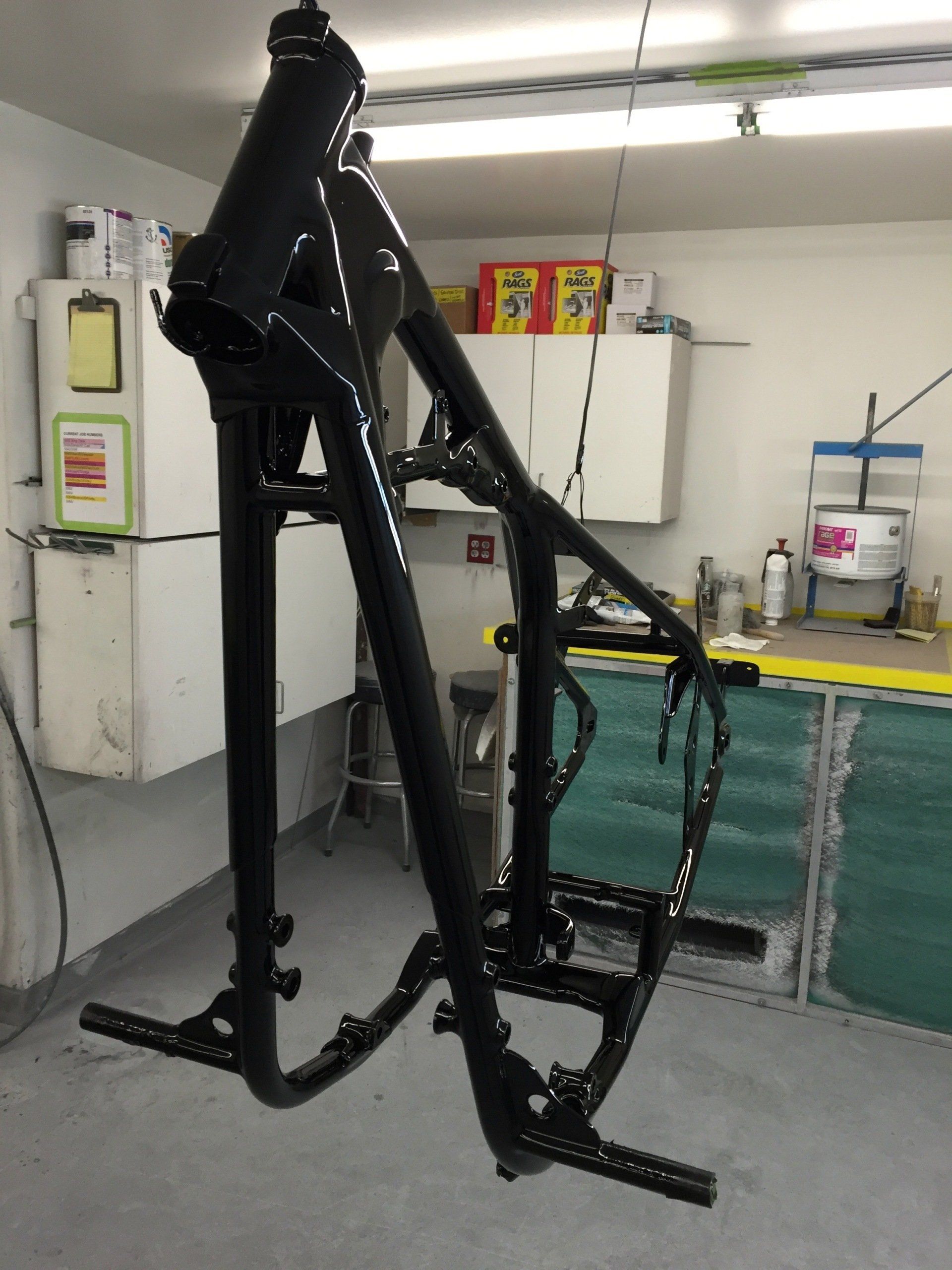 Black metal bicycle frame in a workshop, mounted on a stand with shelves and cabinets in the background