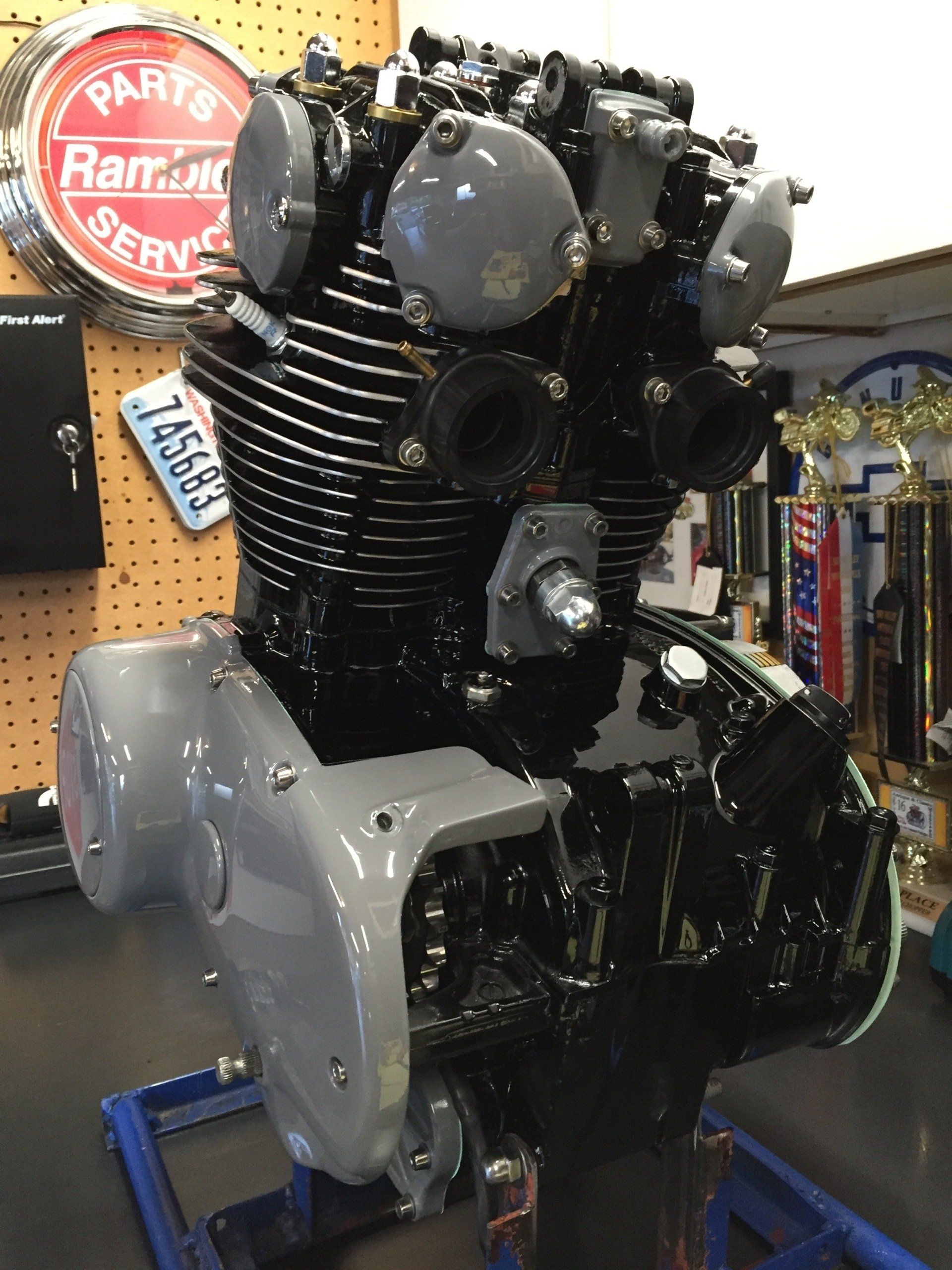 Black motorcycle engine on display in a shop, with gray side covers and a pegboard wall behind it