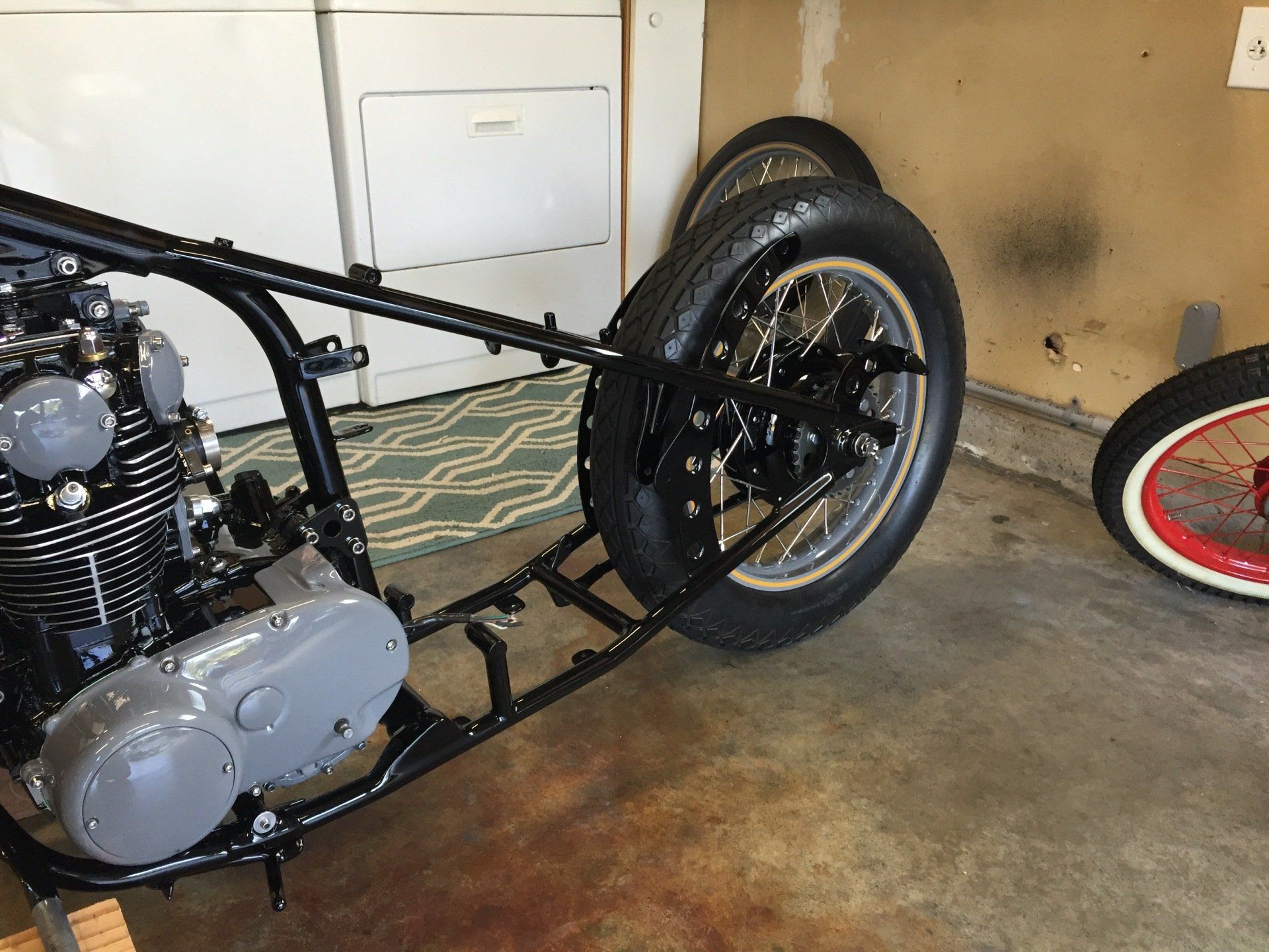 Custom black motorcycle frame in a garage, with exposed engine and rear wheel assembly.