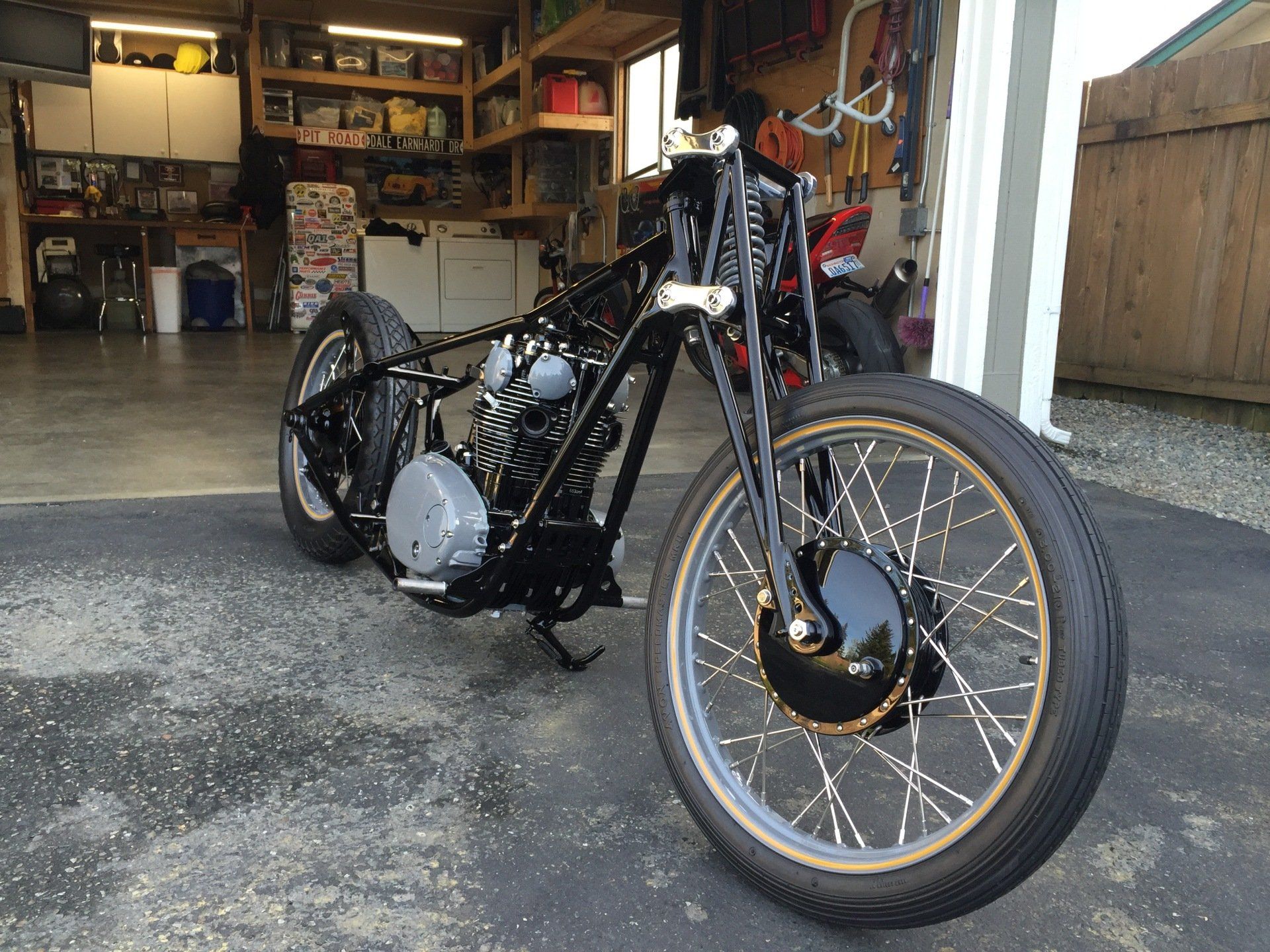 Custom black motorcycle with tan front tire parked in a garage.