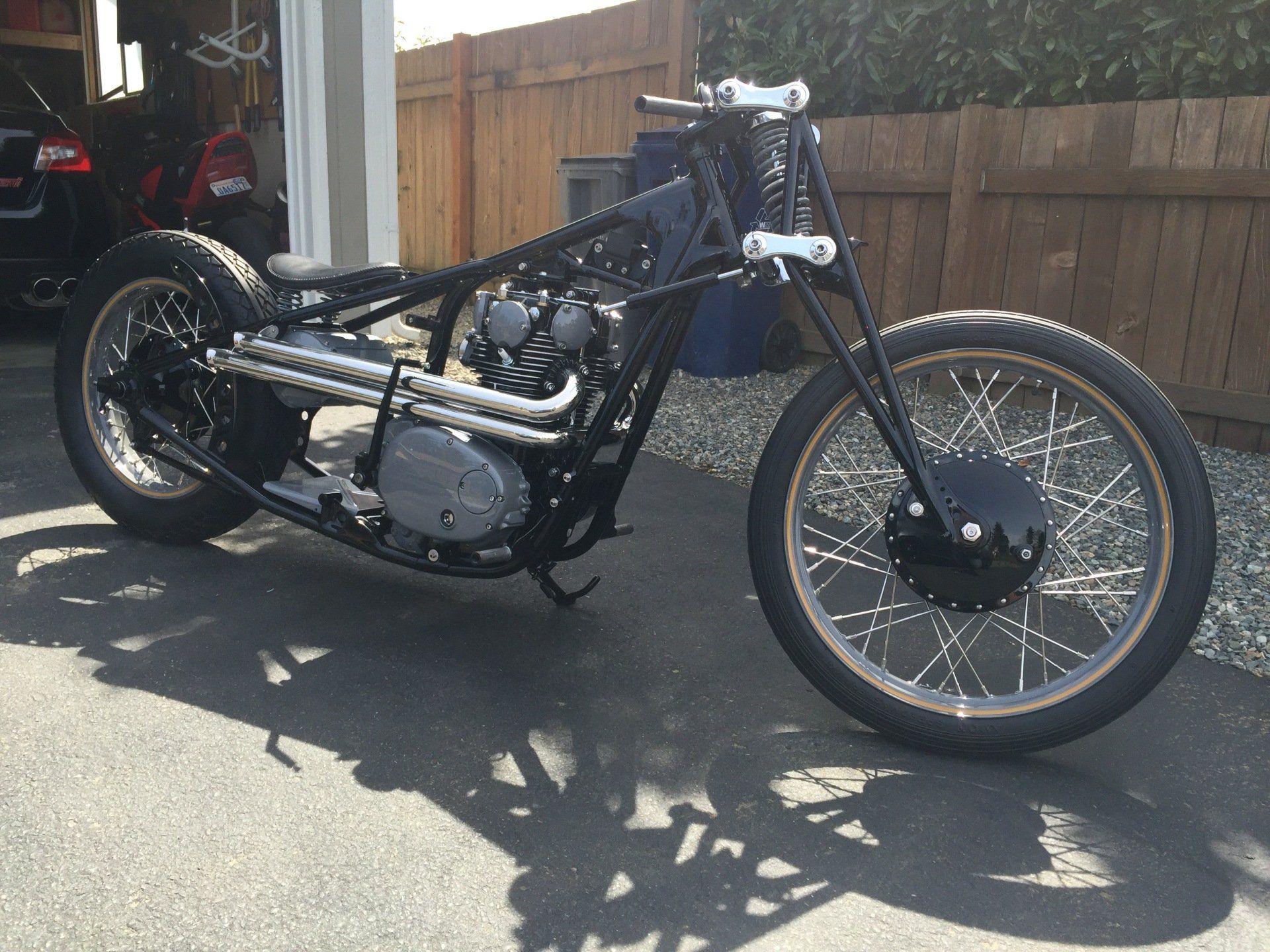 Custom black motorcycle parked on a driveway beside a wooden fence