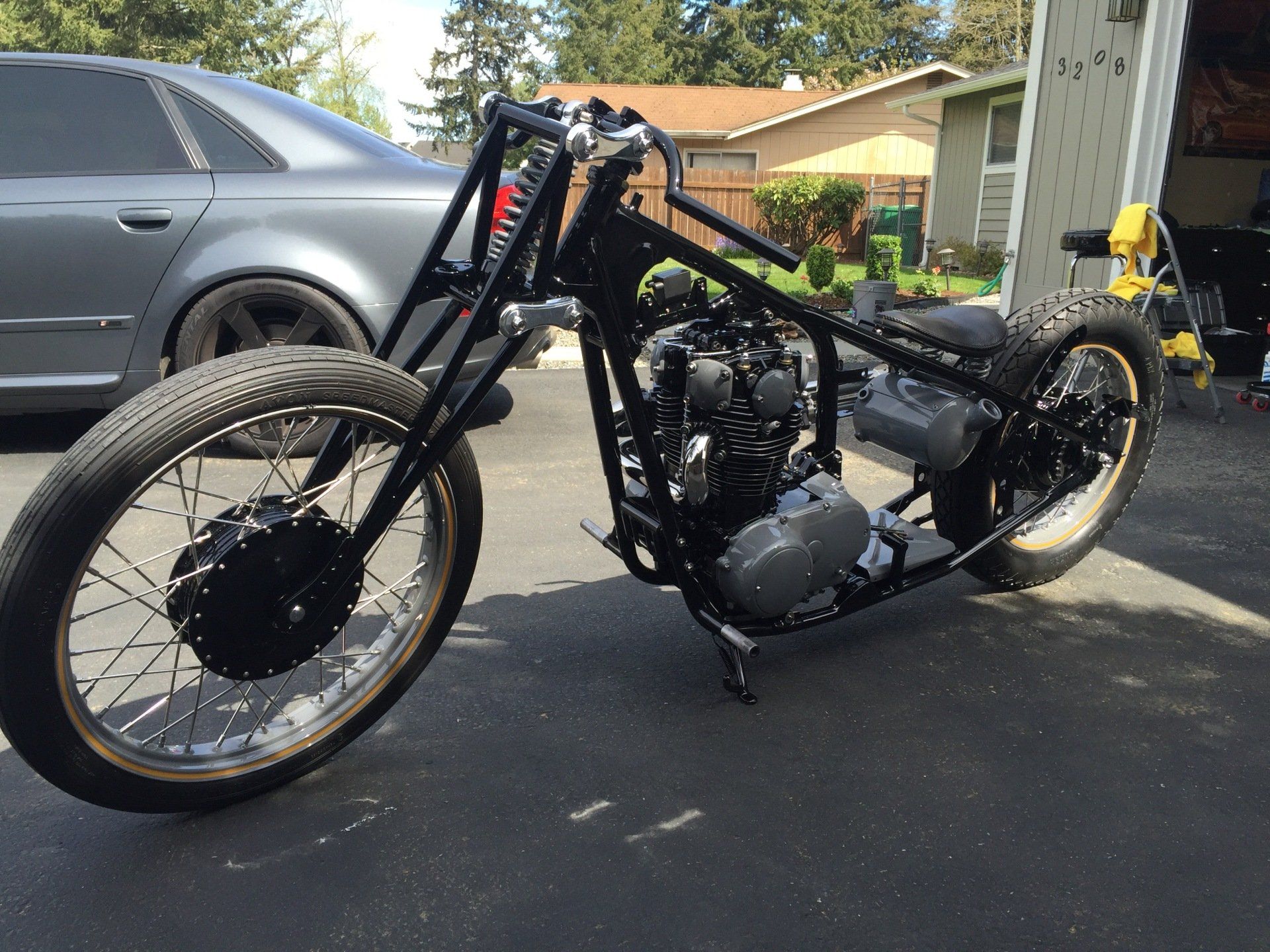 Black custom motorcycle parked in a driveway beside a gray SUV and house