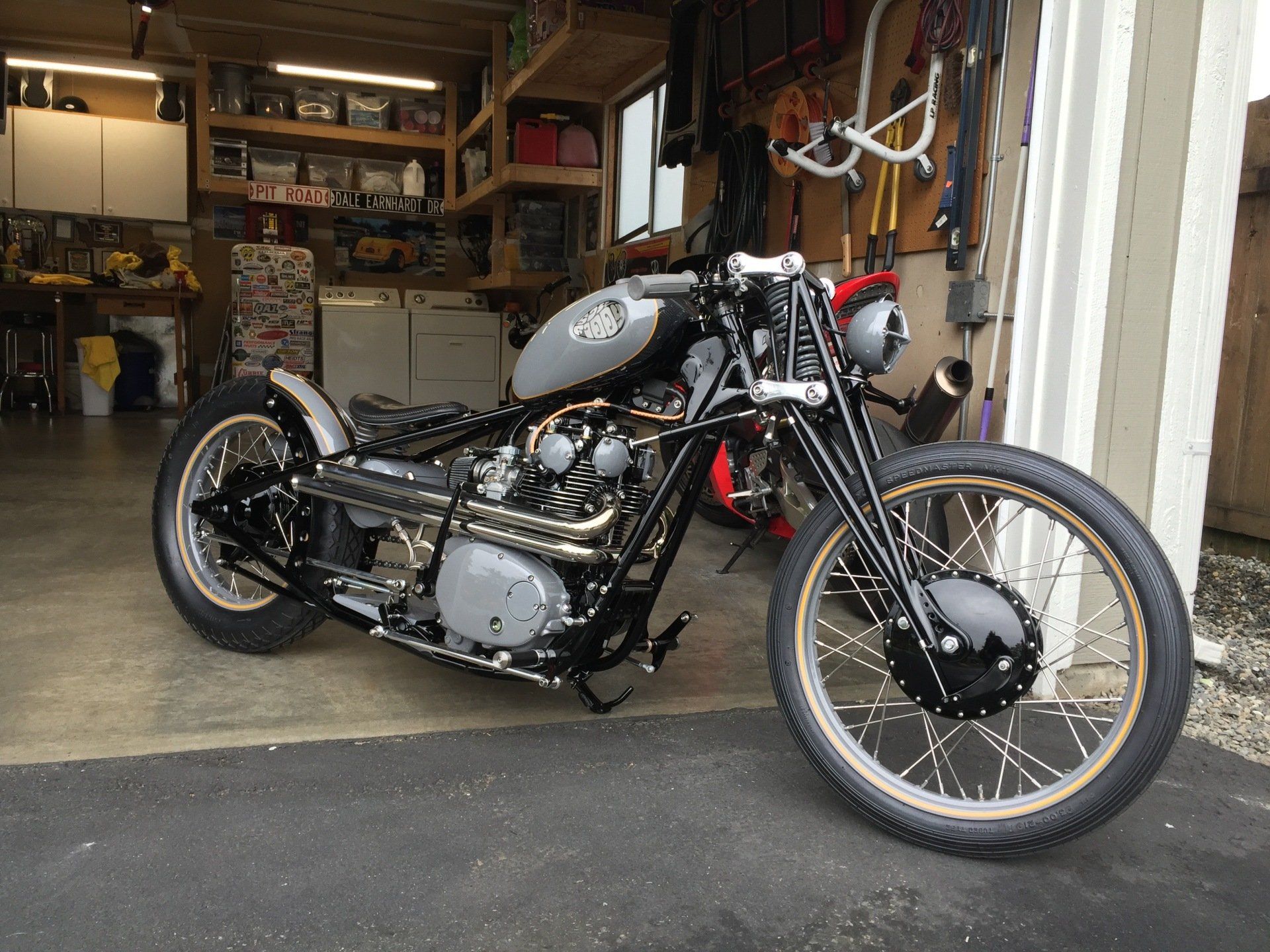 Custom black motorcycle parked in an open garage with shelves and tools in the background