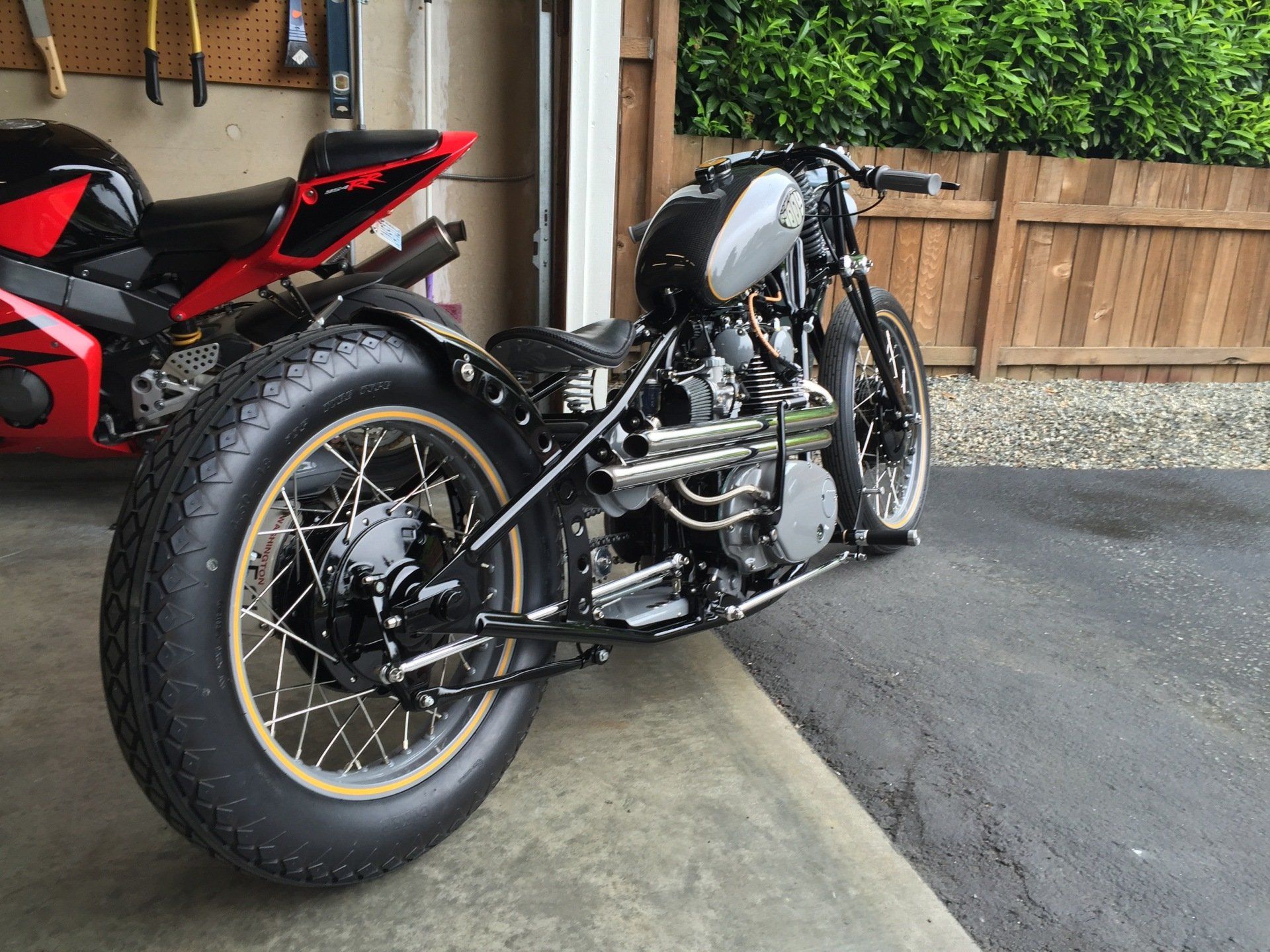 Custom black-and-white motorcycle parked in a driveway beside a red sports bike and wooden fence.