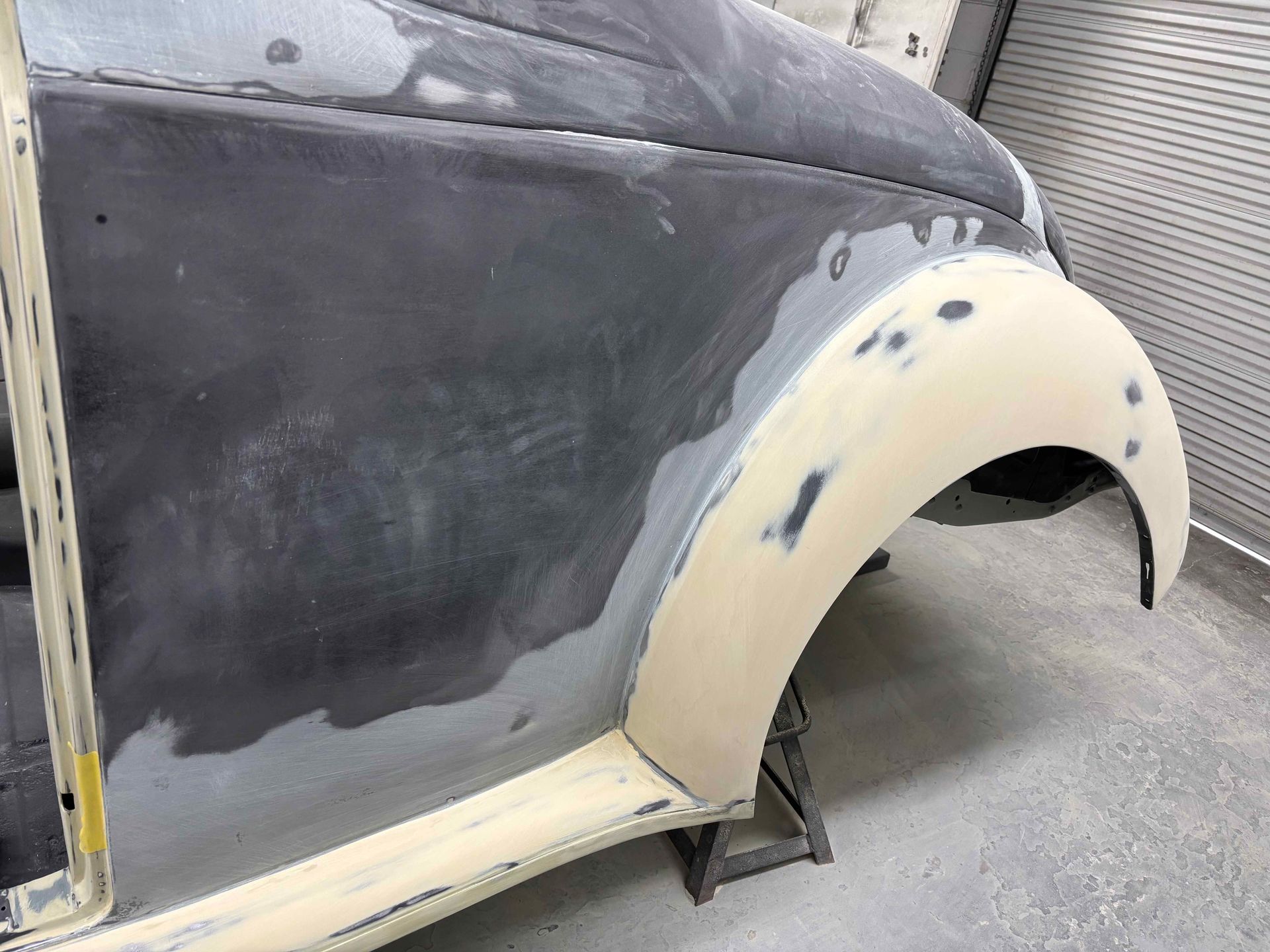 Partially sanded vintage car body with beige wheel arch primer in a workshop
