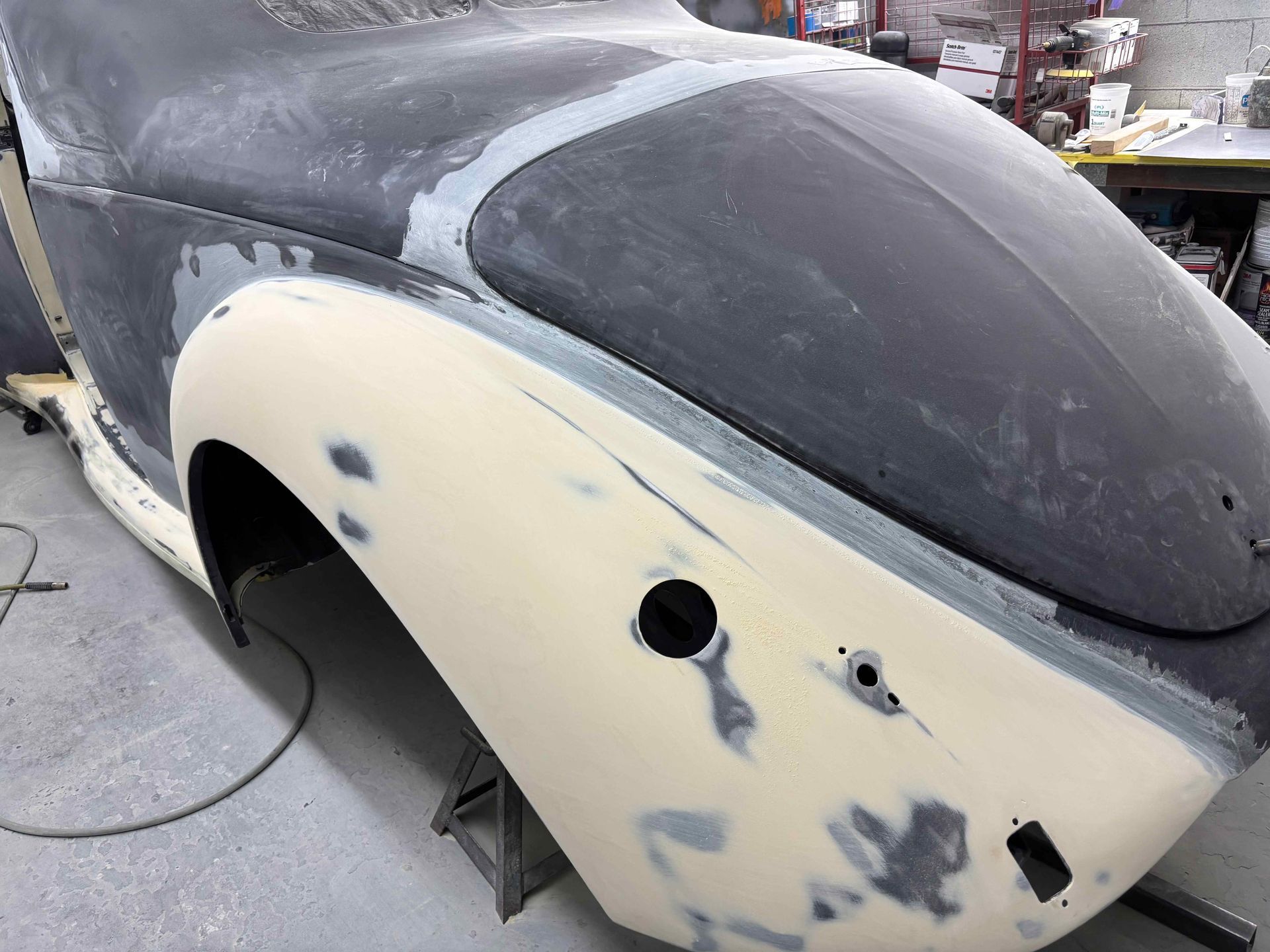 Primed car body panel in a workshop, with sanding marks and cutout holes.