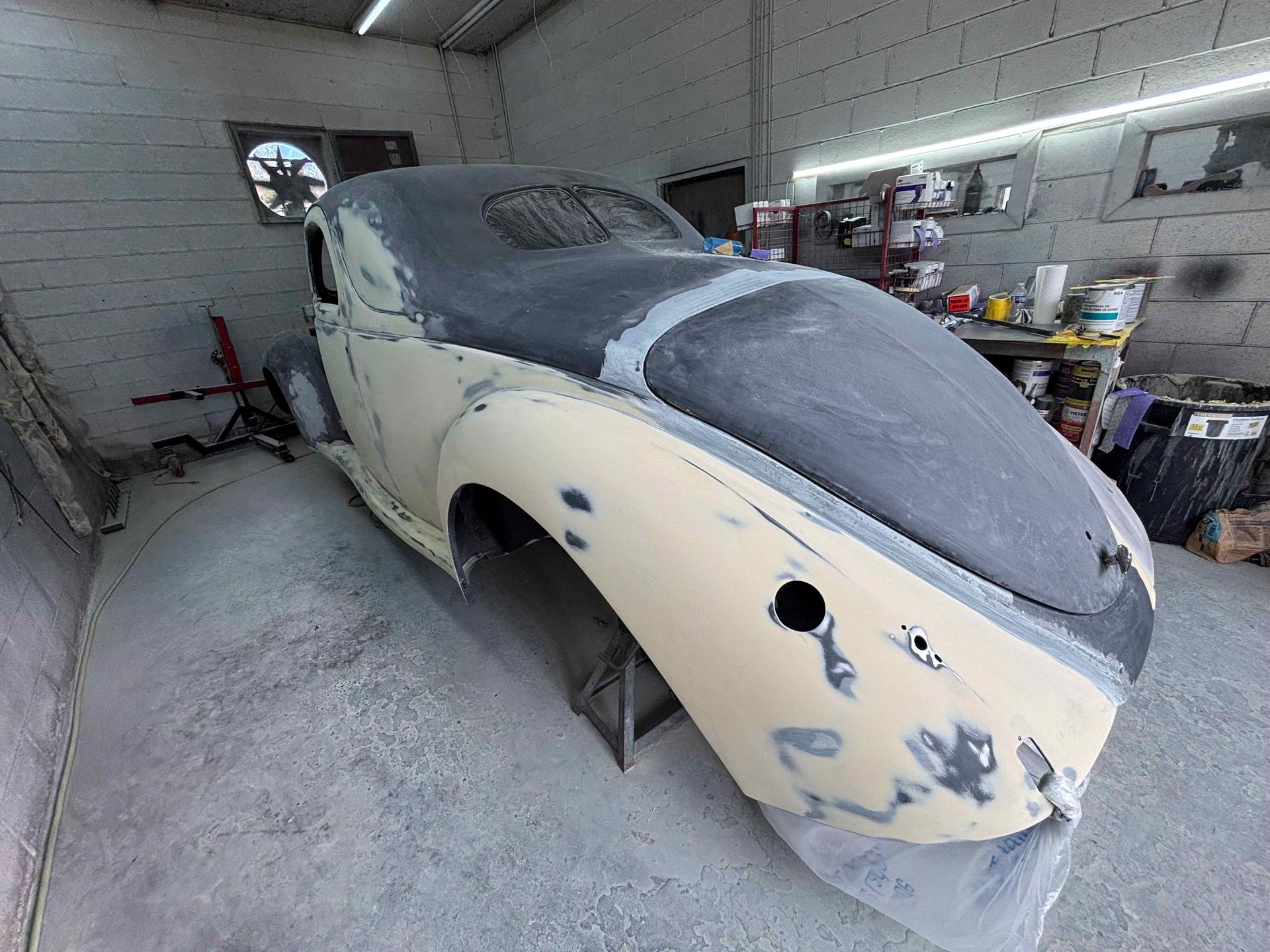 Partially restored beige car body in a workshop, covered with primer and dust