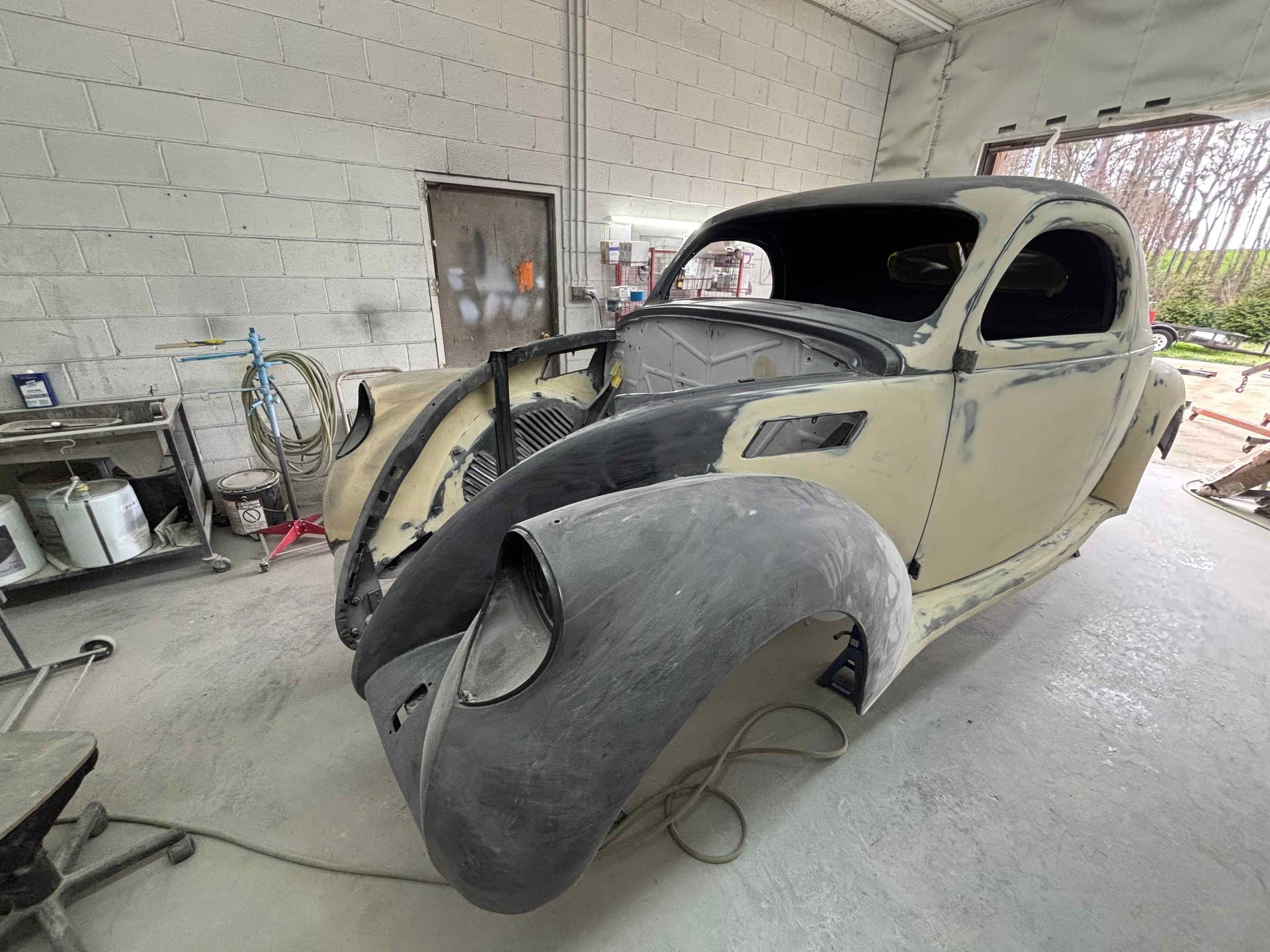 Vintage car body in a garage, partly disassembled with a large curved hood panel leaning against it