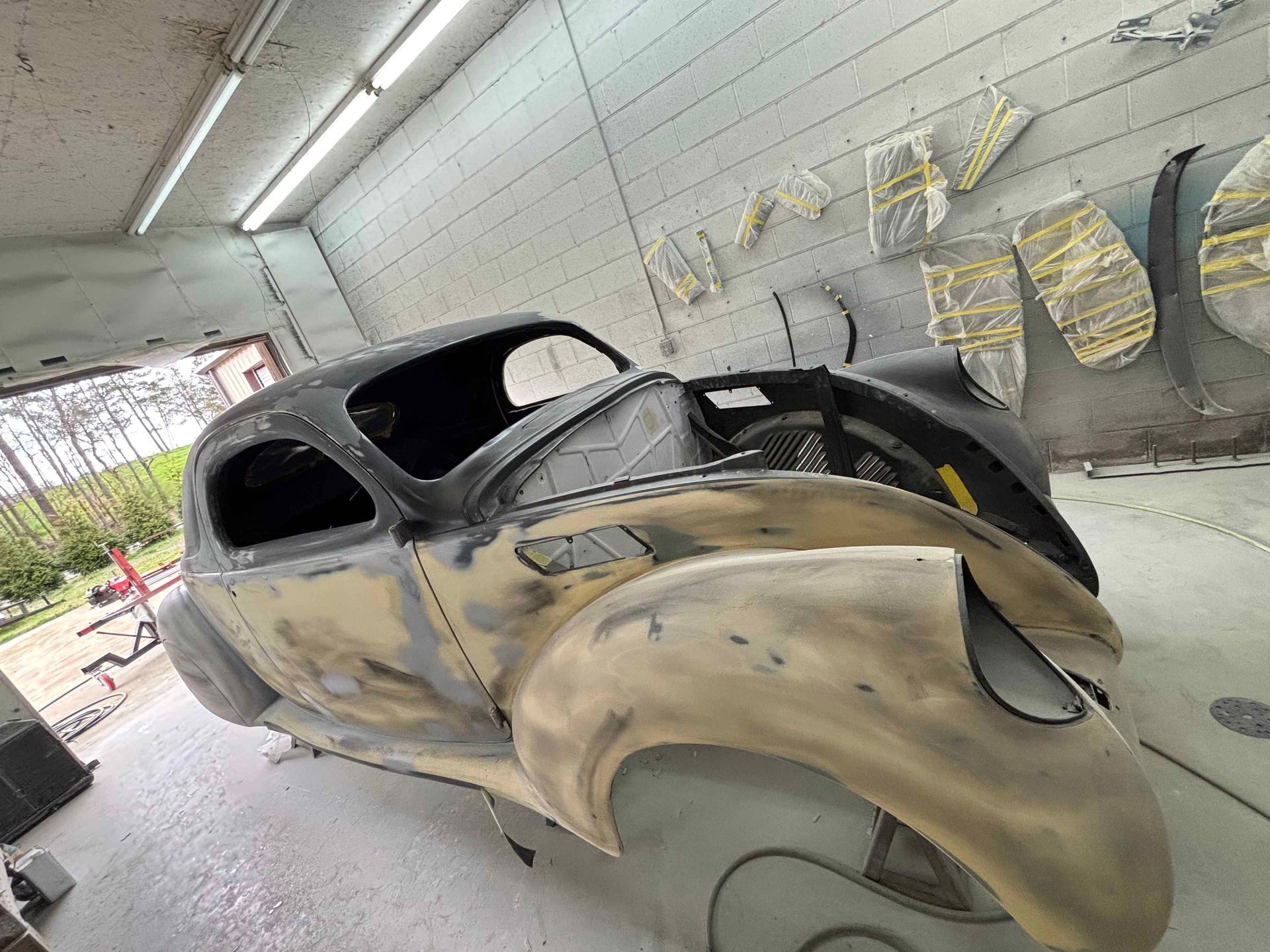 Classic car body in primer inside a workshop, with a beige front panel and black roof.