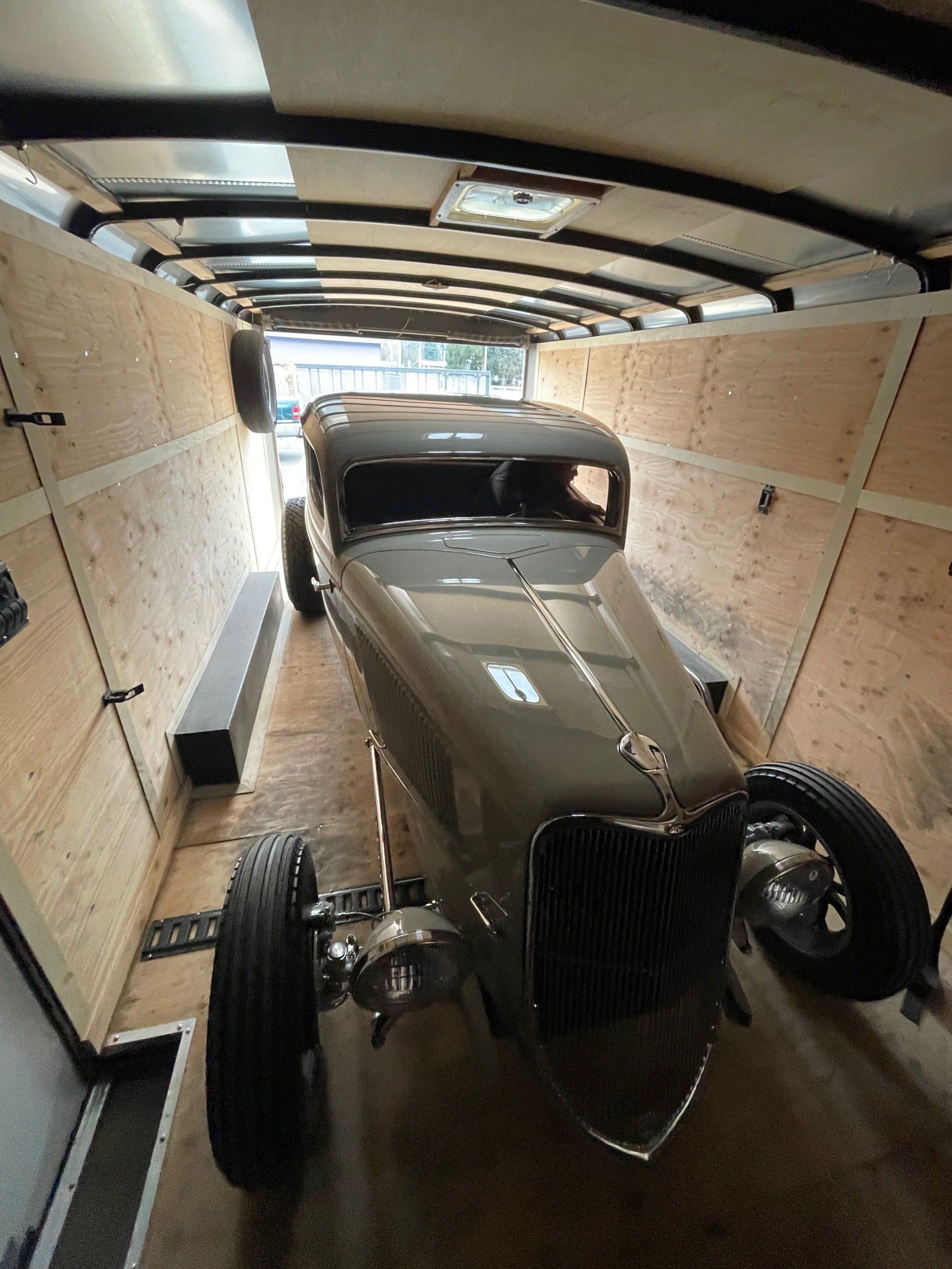 Classic brown vintage car secured inside a covered trailer.