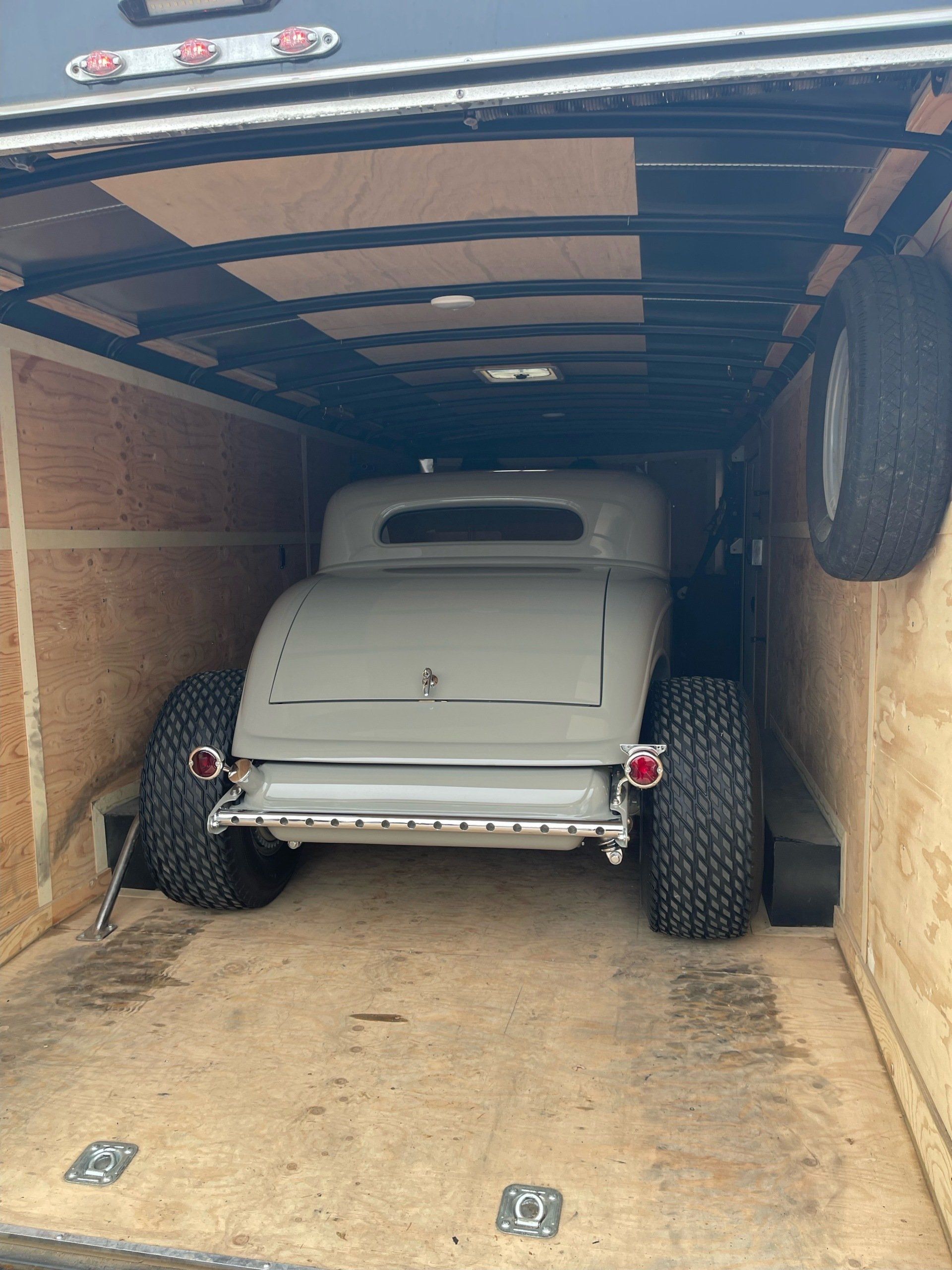 Vintage gray hot rod parked inside a trailer, seen from the open rear door.