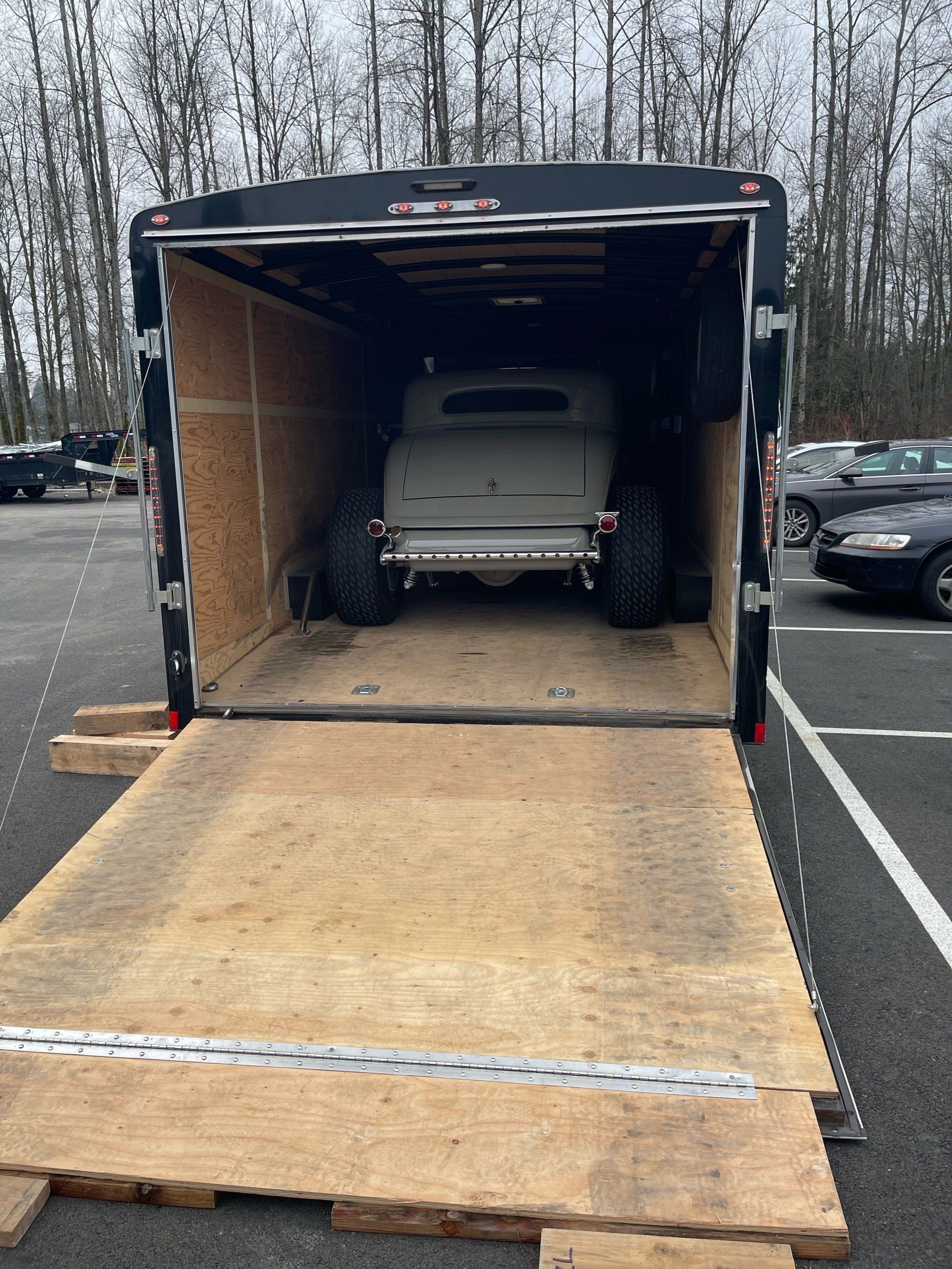 Open trailer with ramp lowered, revealing a classic car inside in a parking lot.