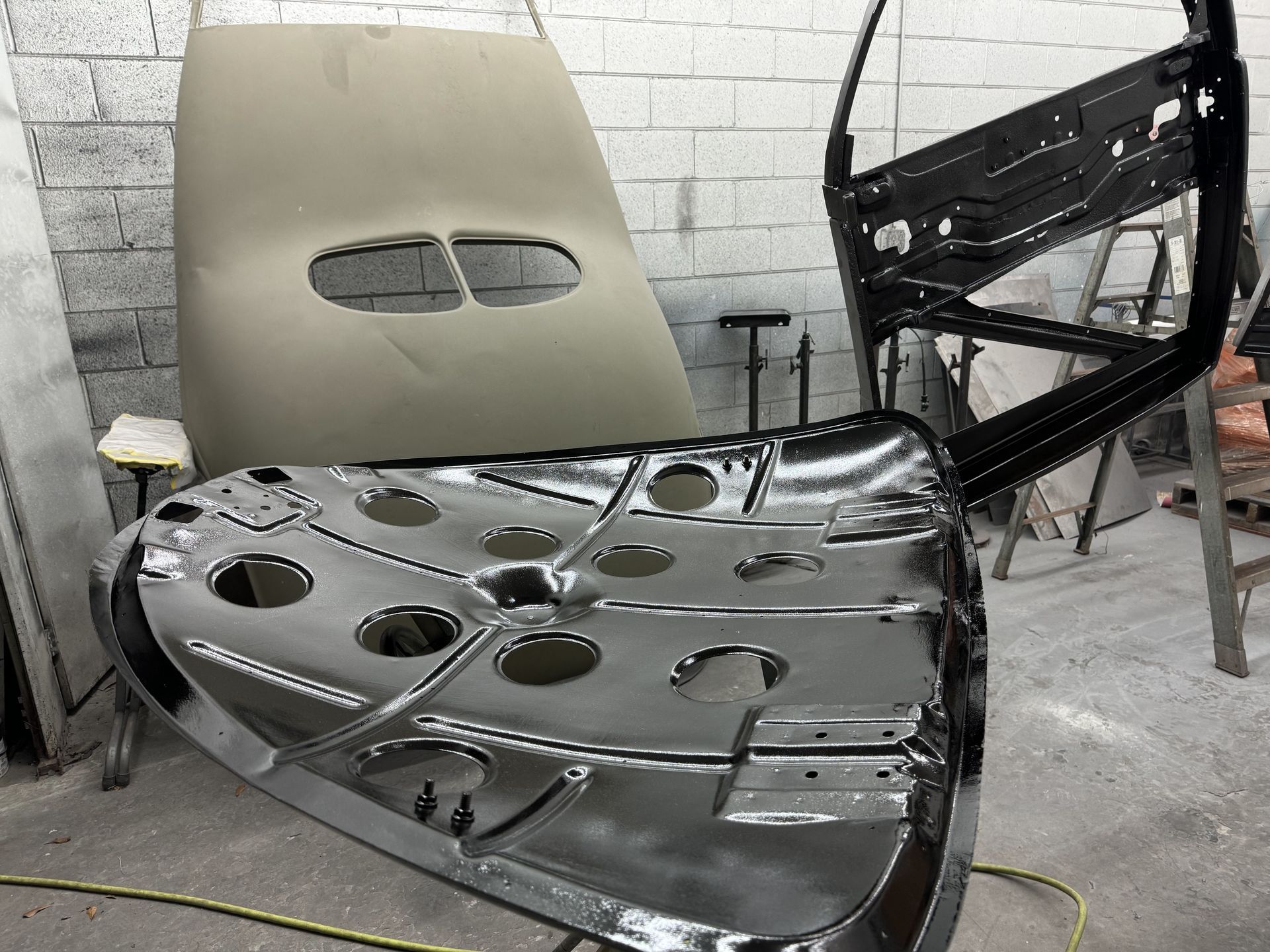 Shiny black car hood with cutout holes leaning against a beige seat in a workshop