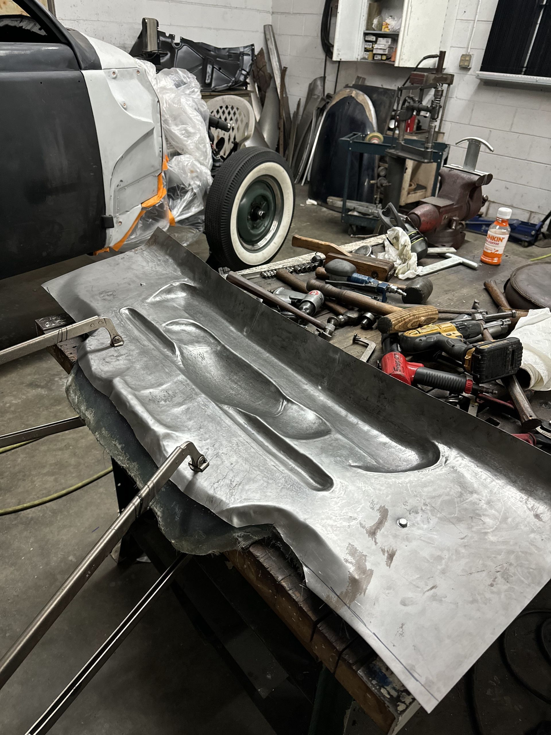 Silver car body panel in a workshop, with tools and parts scattered on the floor.