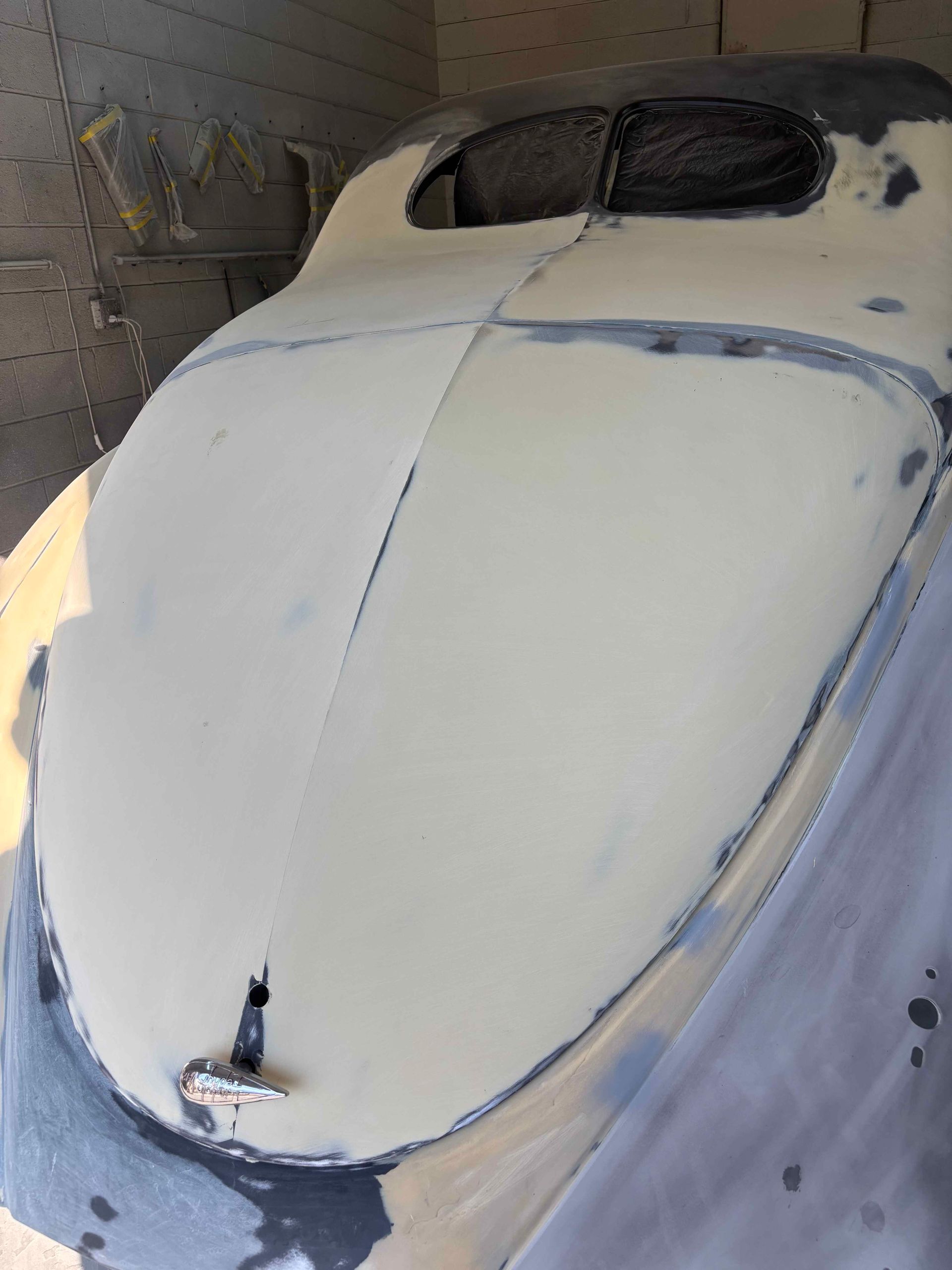 White car body in primer inside a workshop, viewed from above with windows and edges masked off