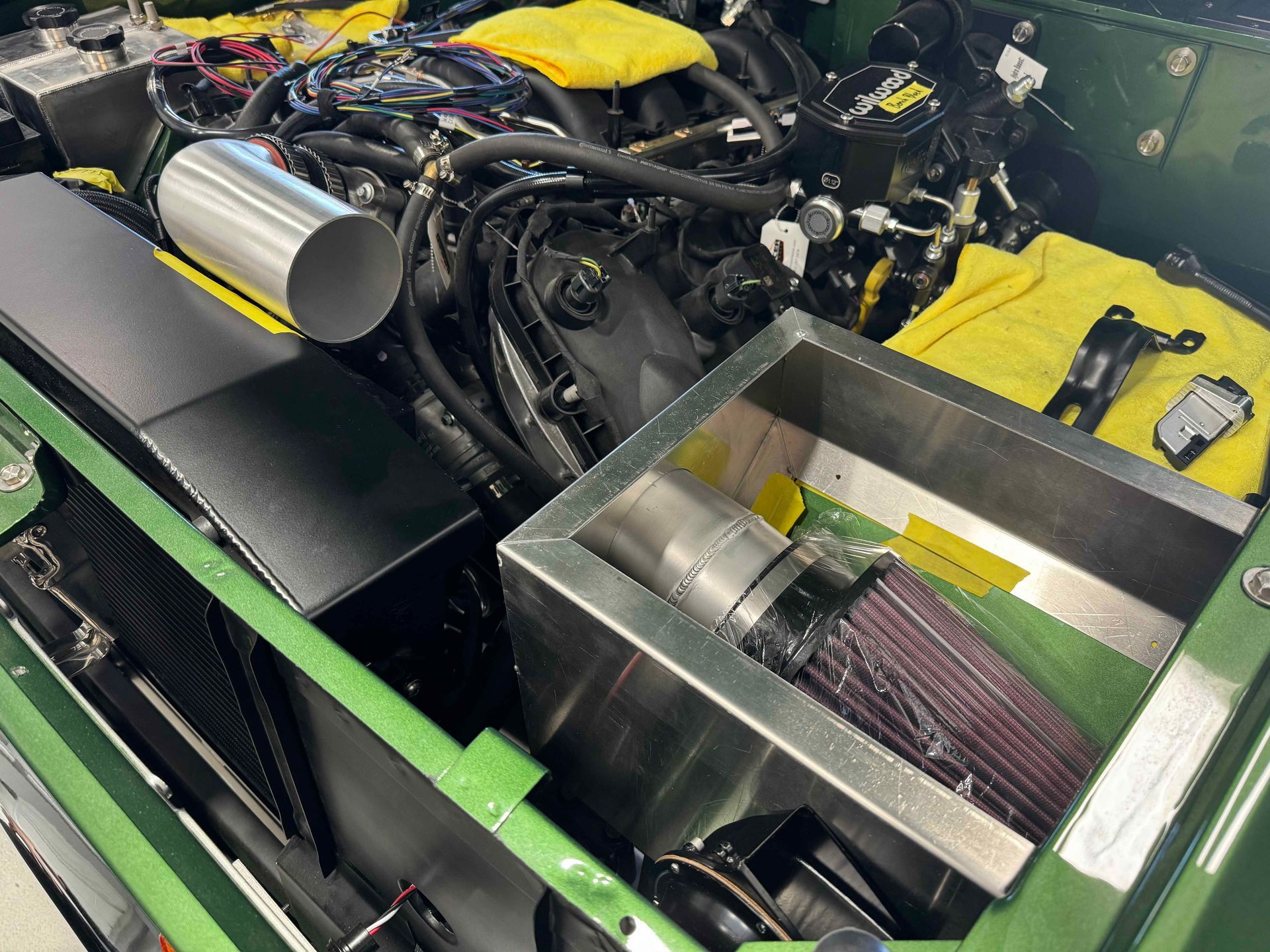 Car engine bay with polished intake pipes, exposed components, and a yellow cloth in a workshop setting