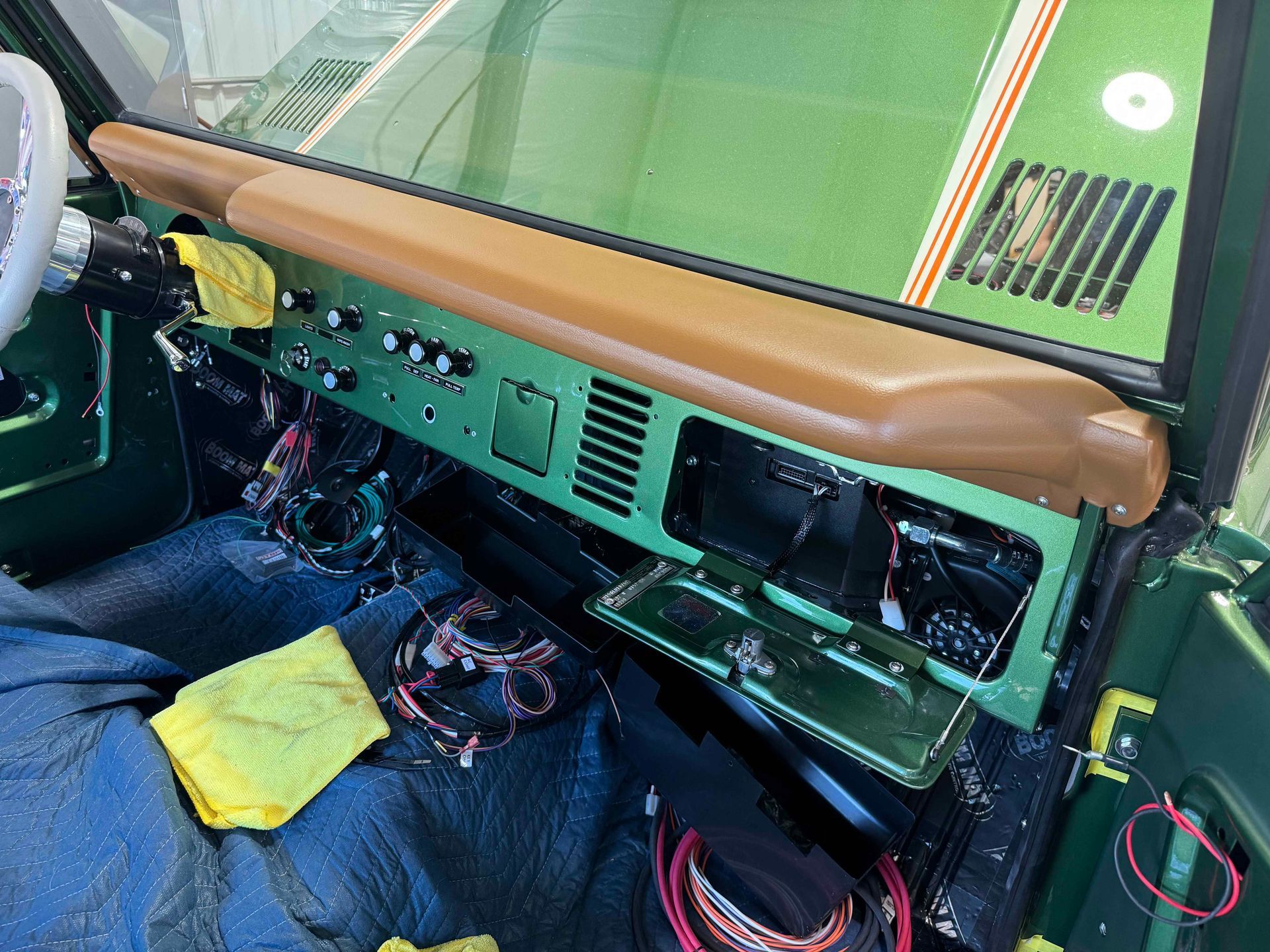 Classic car dashboard and tan bench seat with exposed wiring and blue seat cover inside the cabin.