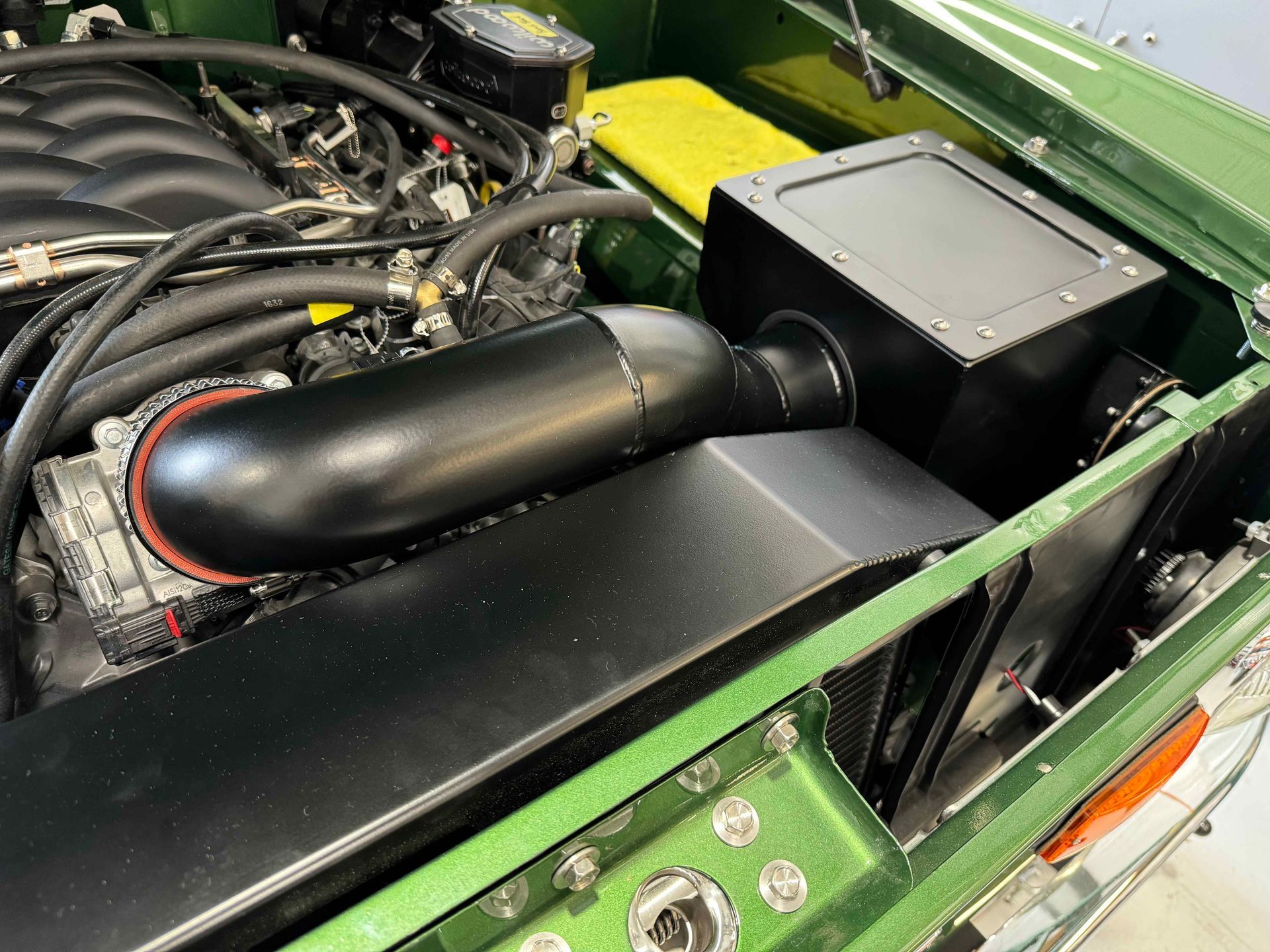 Black intake tube and box in a green engine bay, with hoses and mechanical components visible