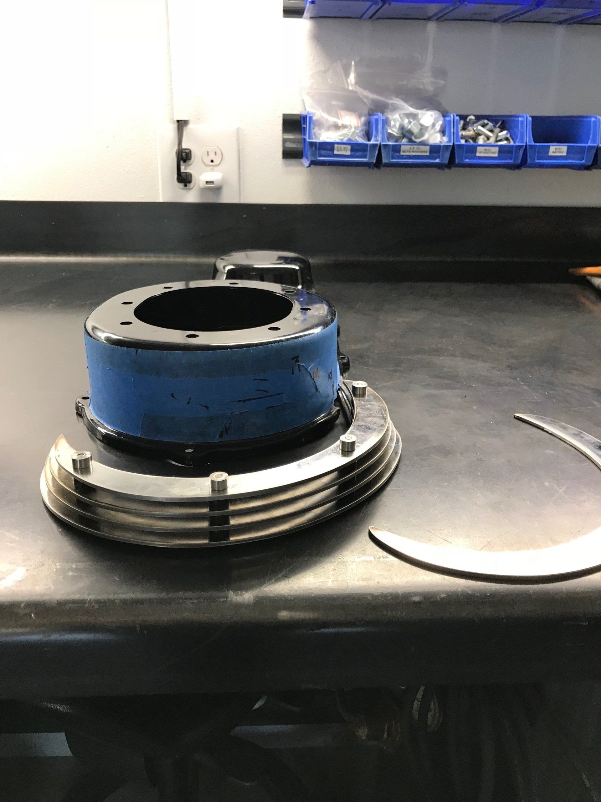Blue metal mechanical part on a workbench with a detached curved metal piece nearby.