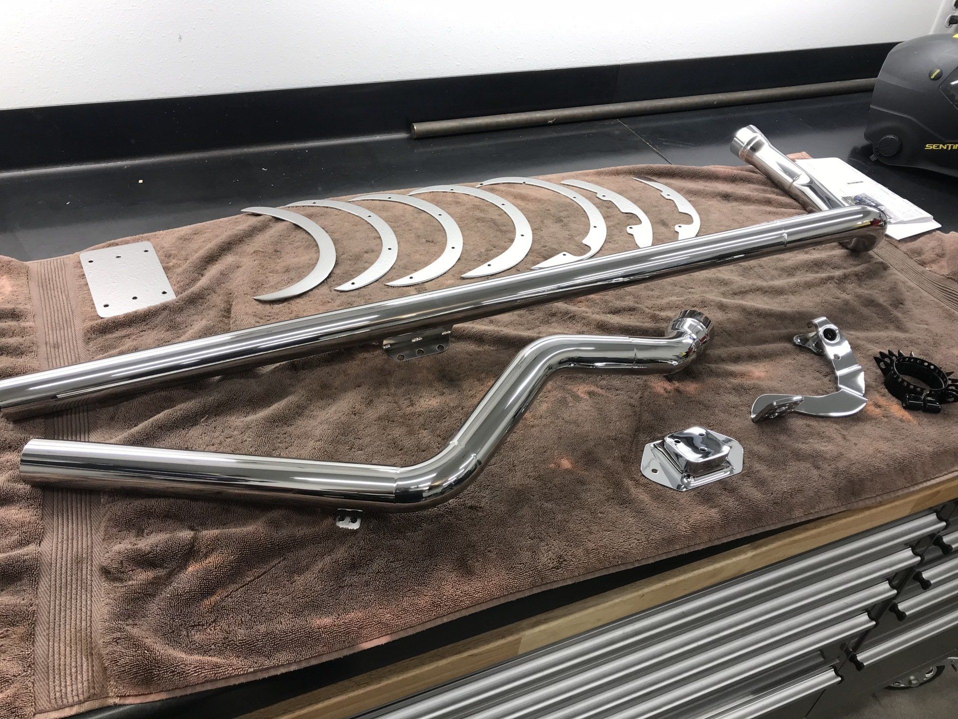 Chrome motorcycle exhaust pipes and hardware laid out on a brown towel on a workbench