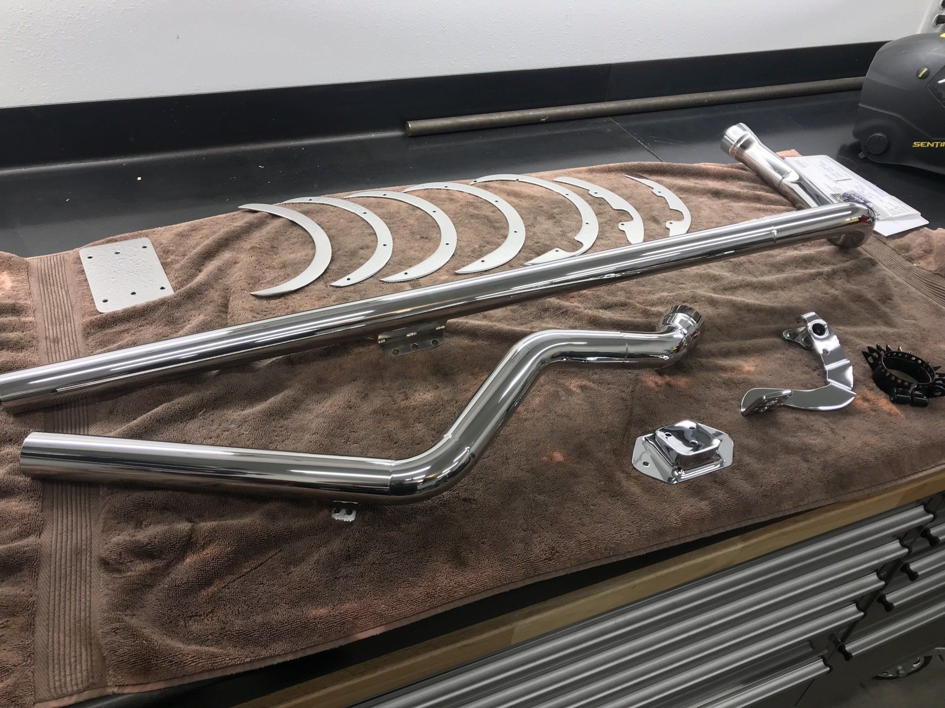 Chrome motorcycle exhaust pipes and small parts laid out on a brown towel over a tool chest